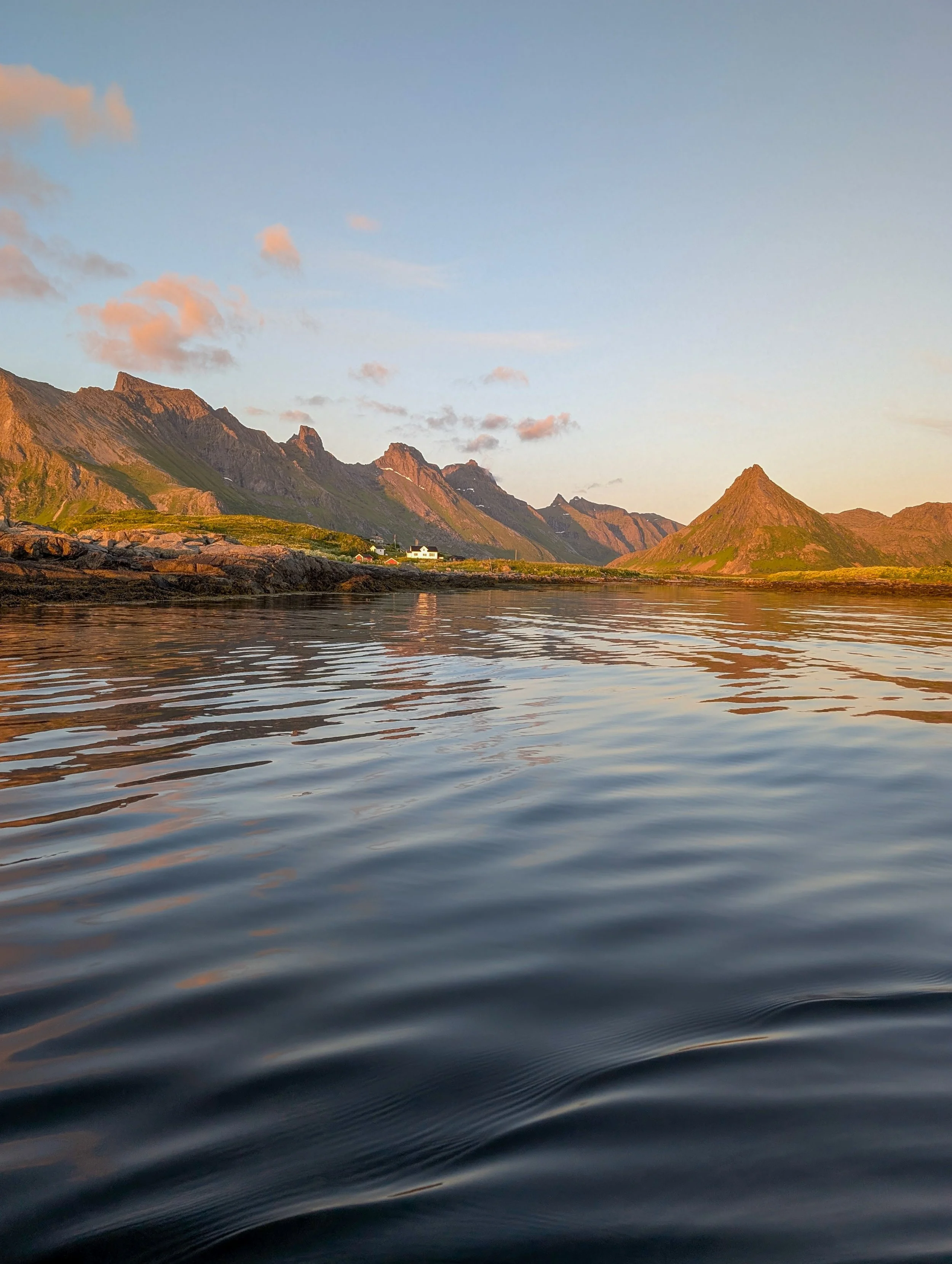 Sunset mountain landscape with a small coastal village and rippling water in the foreground