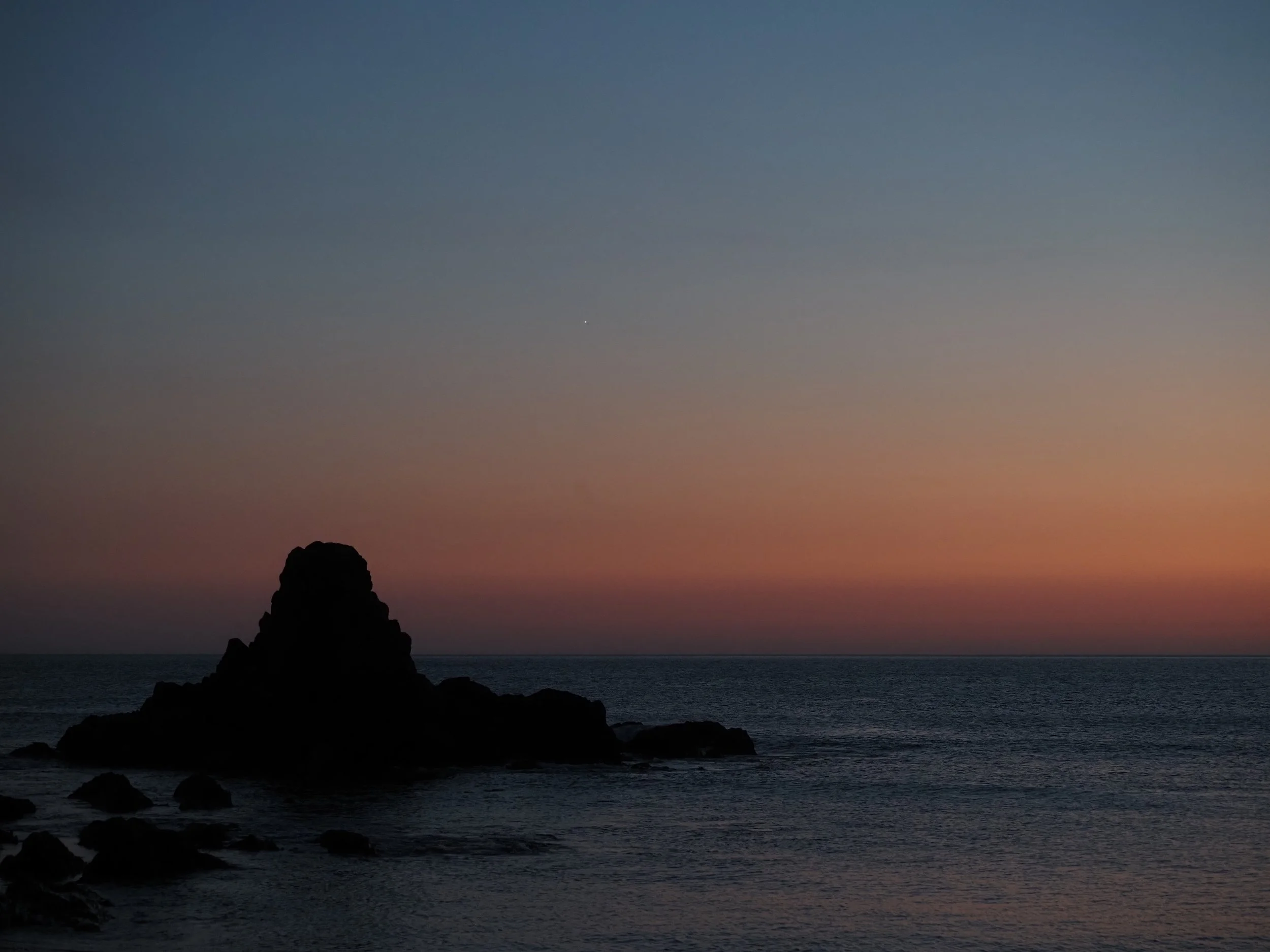 Rocky ocean shoreline silhouetted against a blue and pink sunset sky