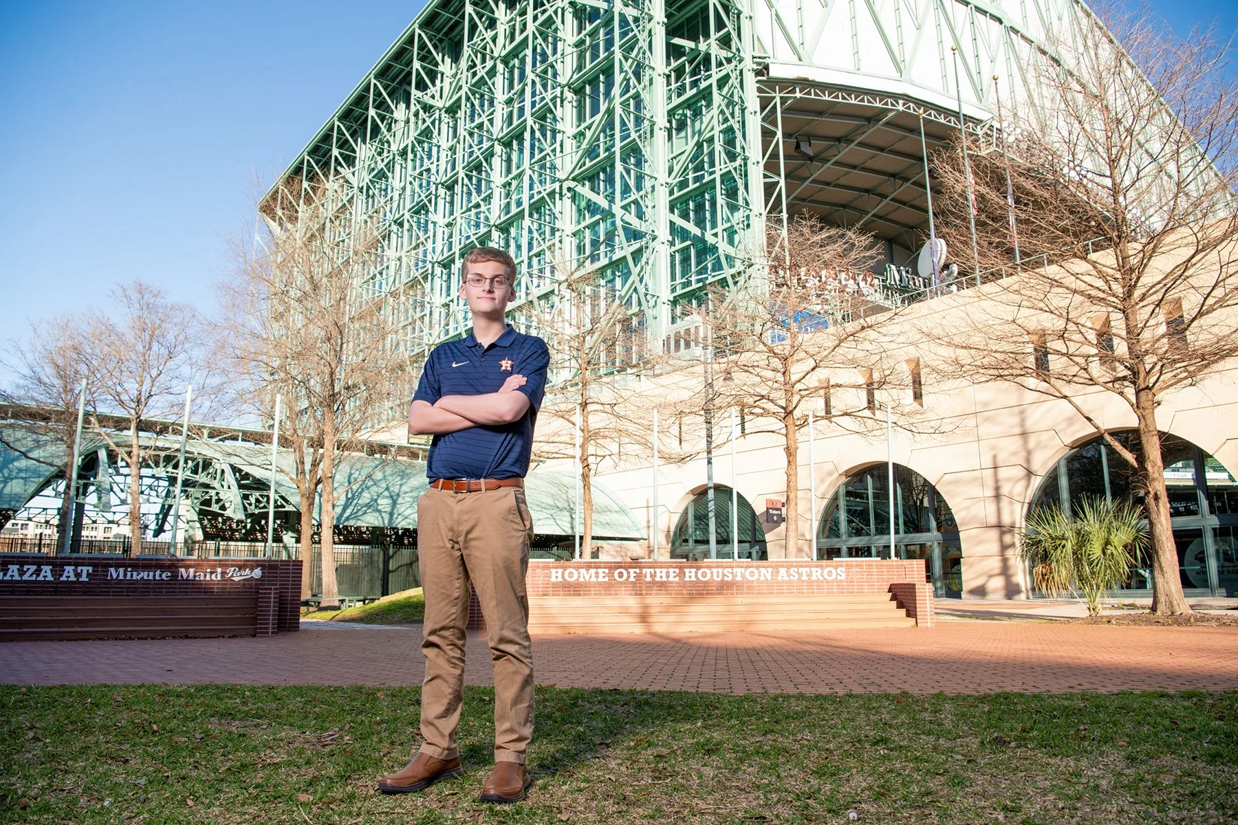 A young man standing with arms crossed in front of the Houston Astros' Minute Maid Park stadium during daytime.