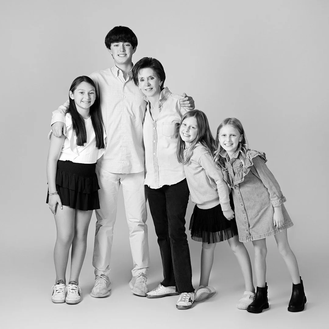 Black and white photo of a family of six, including one adult women and four children standing close together and smiling.