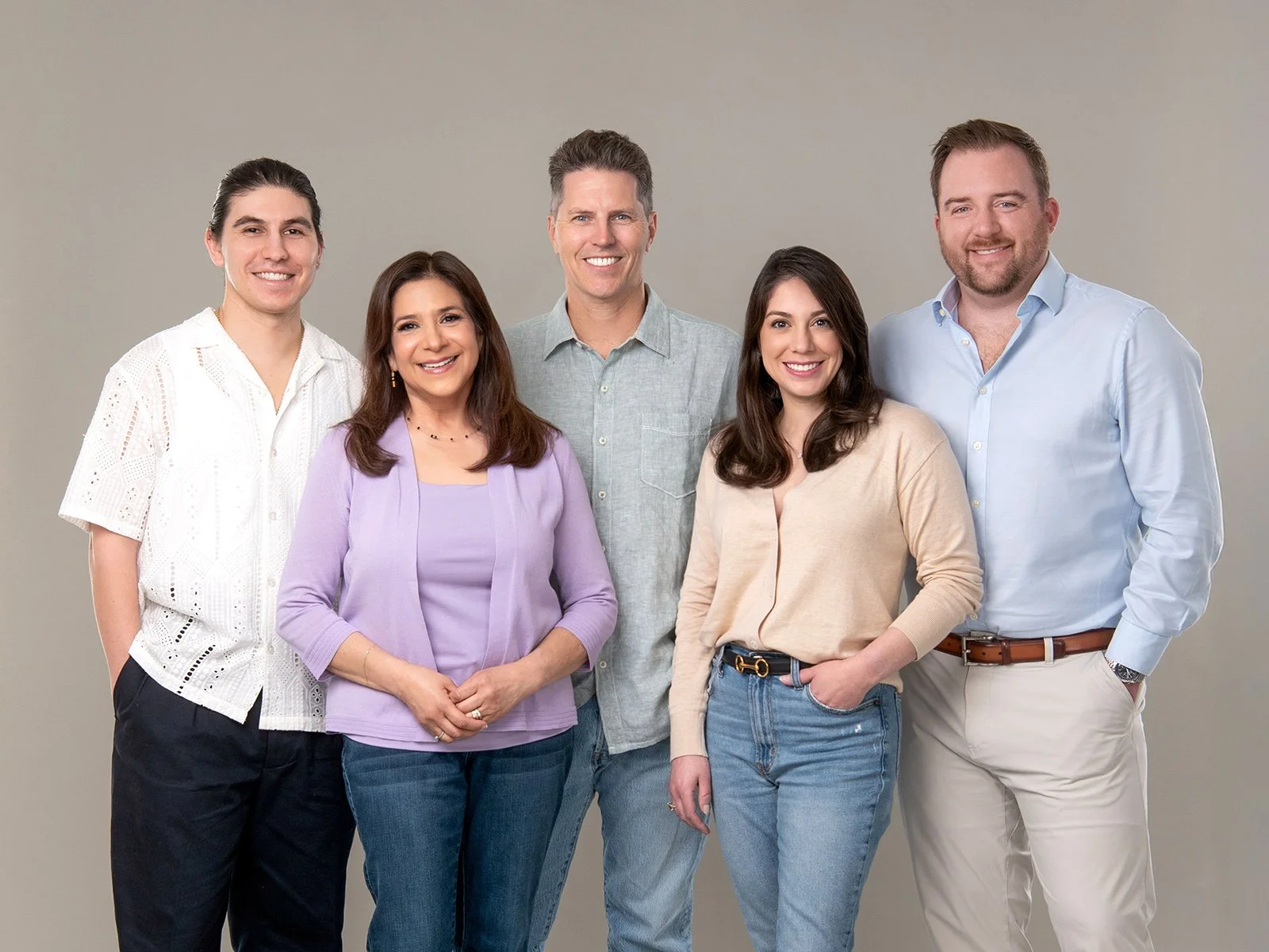 Group of five people smiling and standing together against a plain gray background.