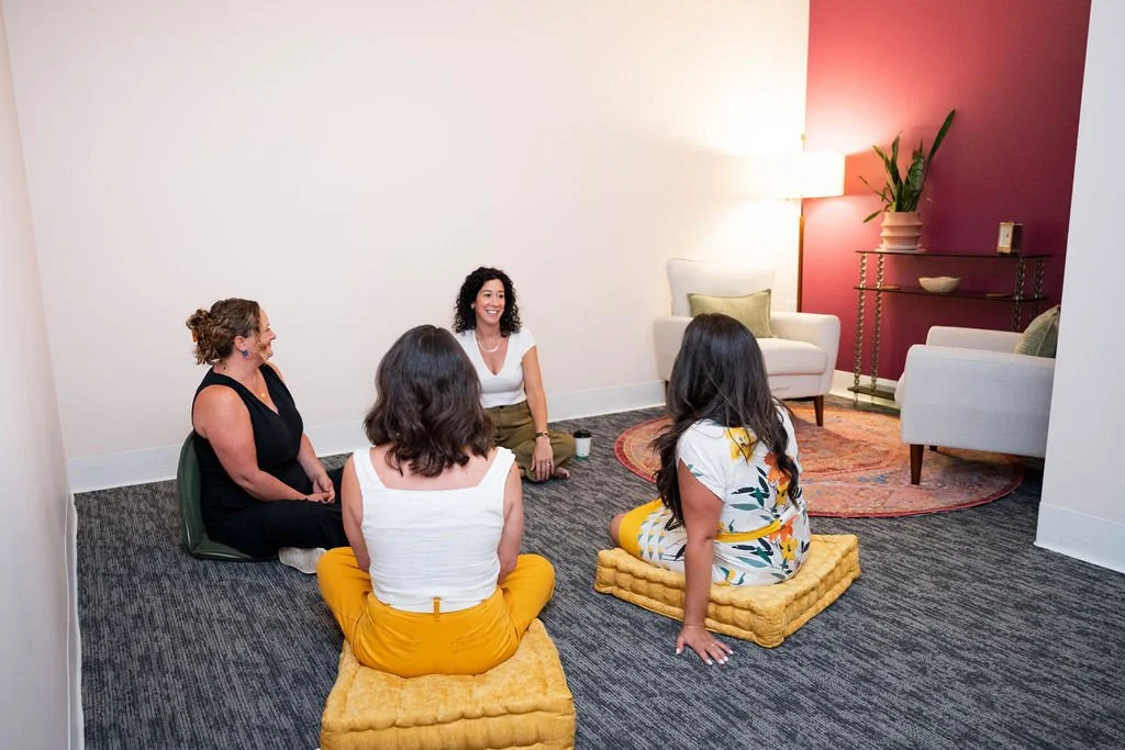 Four women sitting on cushions in a circle in a cozy, modern room having a conversation.