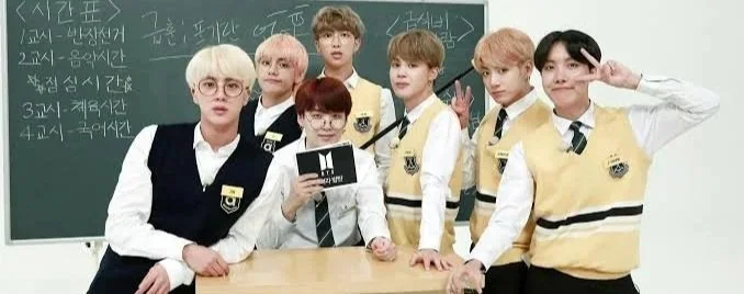 Six young men in school uniforms posing for a photo inside a classroom, with a blackboard in the background.