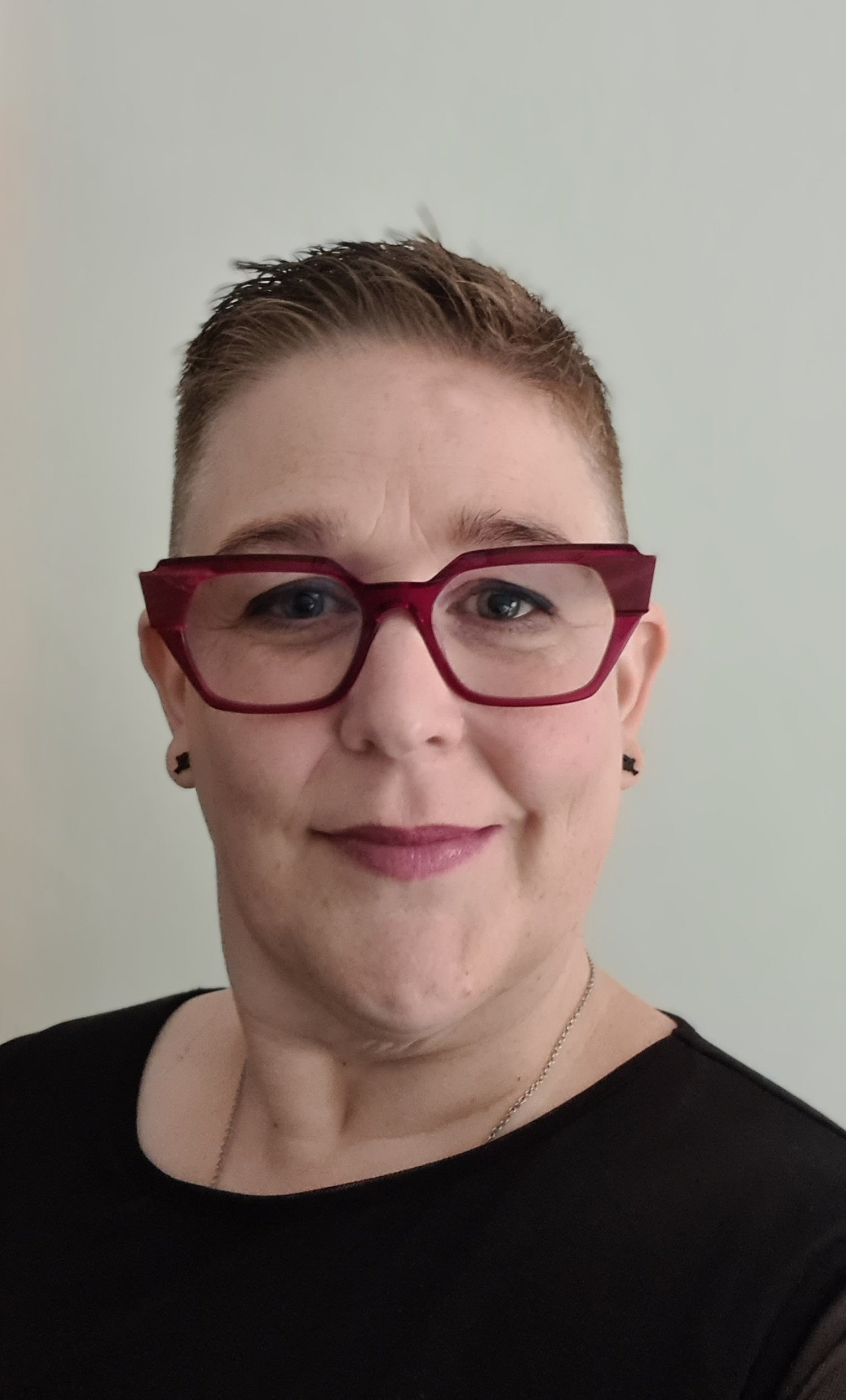Head and shoulders photo of a middle-aged white woman wearing red-framed glasses