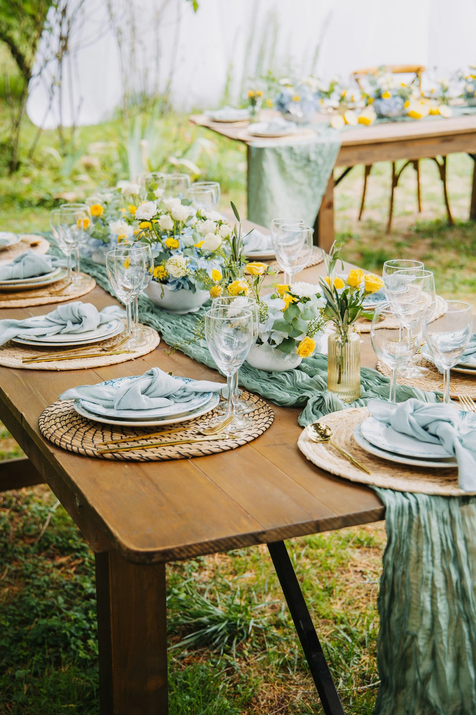 Outdoor dining table set for a meal with floral centerpieces, glassware, and place settings, in a garden or backyard.