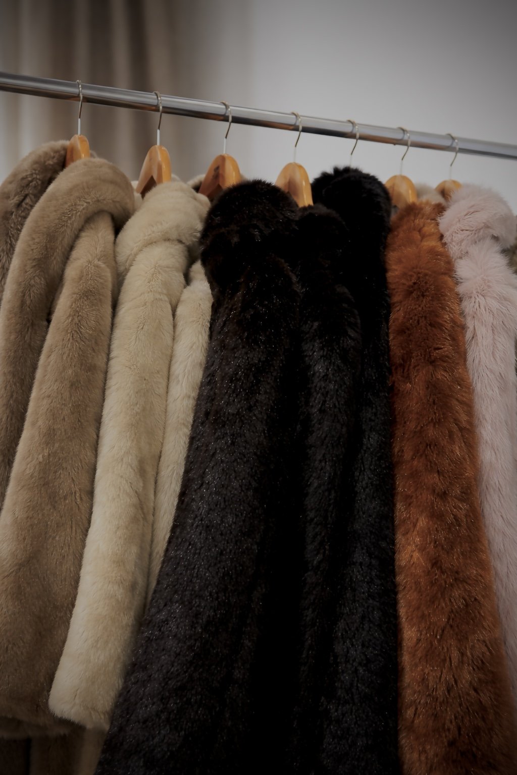 A row of faux fur coats in various colors hanging on a metal clothing rack.
