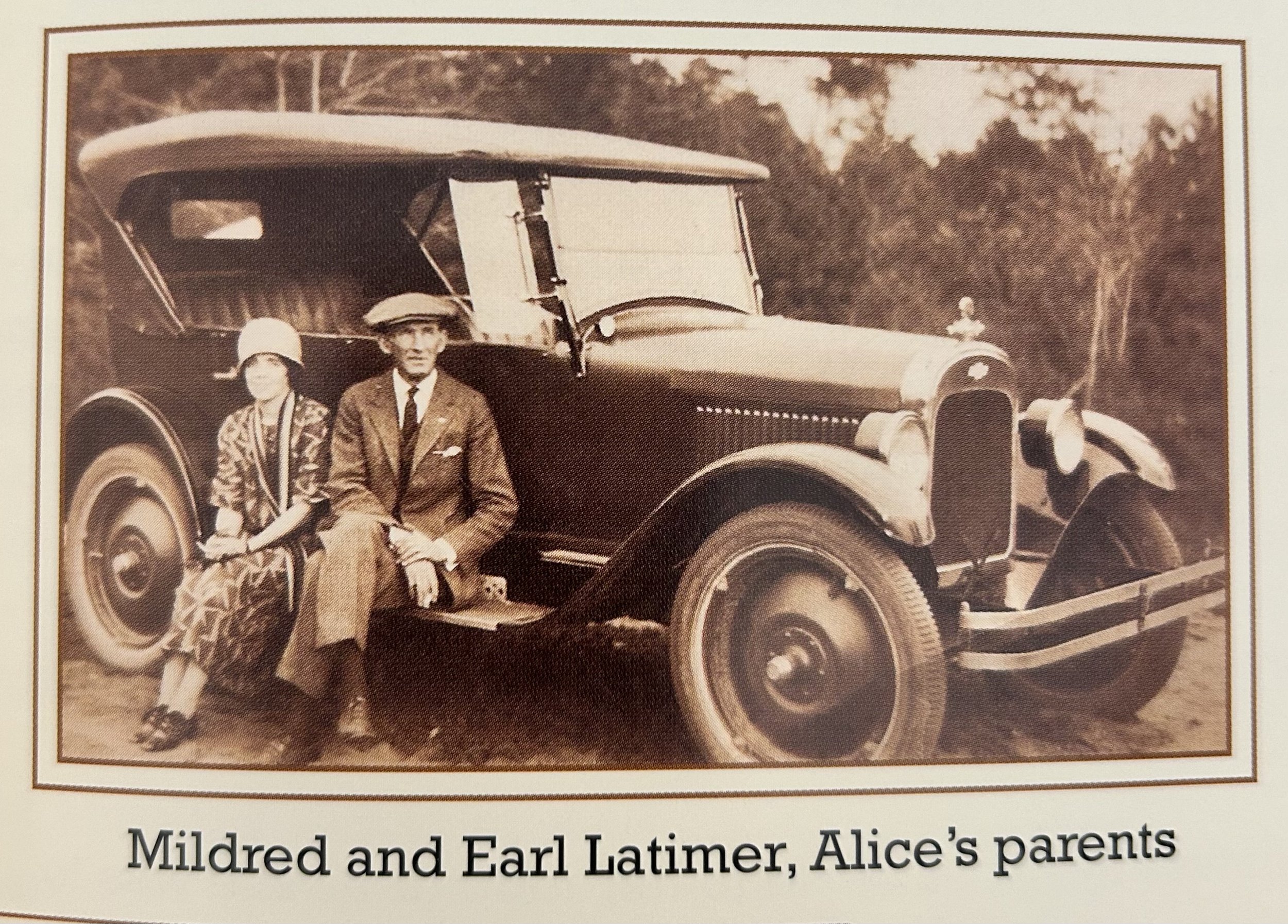 A sepia-toned photograph of a vintage automobile with a woman and a man standing beside it. The woman wears a hat and patterned coat, and the man wears a suit and tie. They are outdoor, with trees in the background. The photo is framed, and a caption underneath reads, "Mildred and Earl Latimer, Alice's parents."