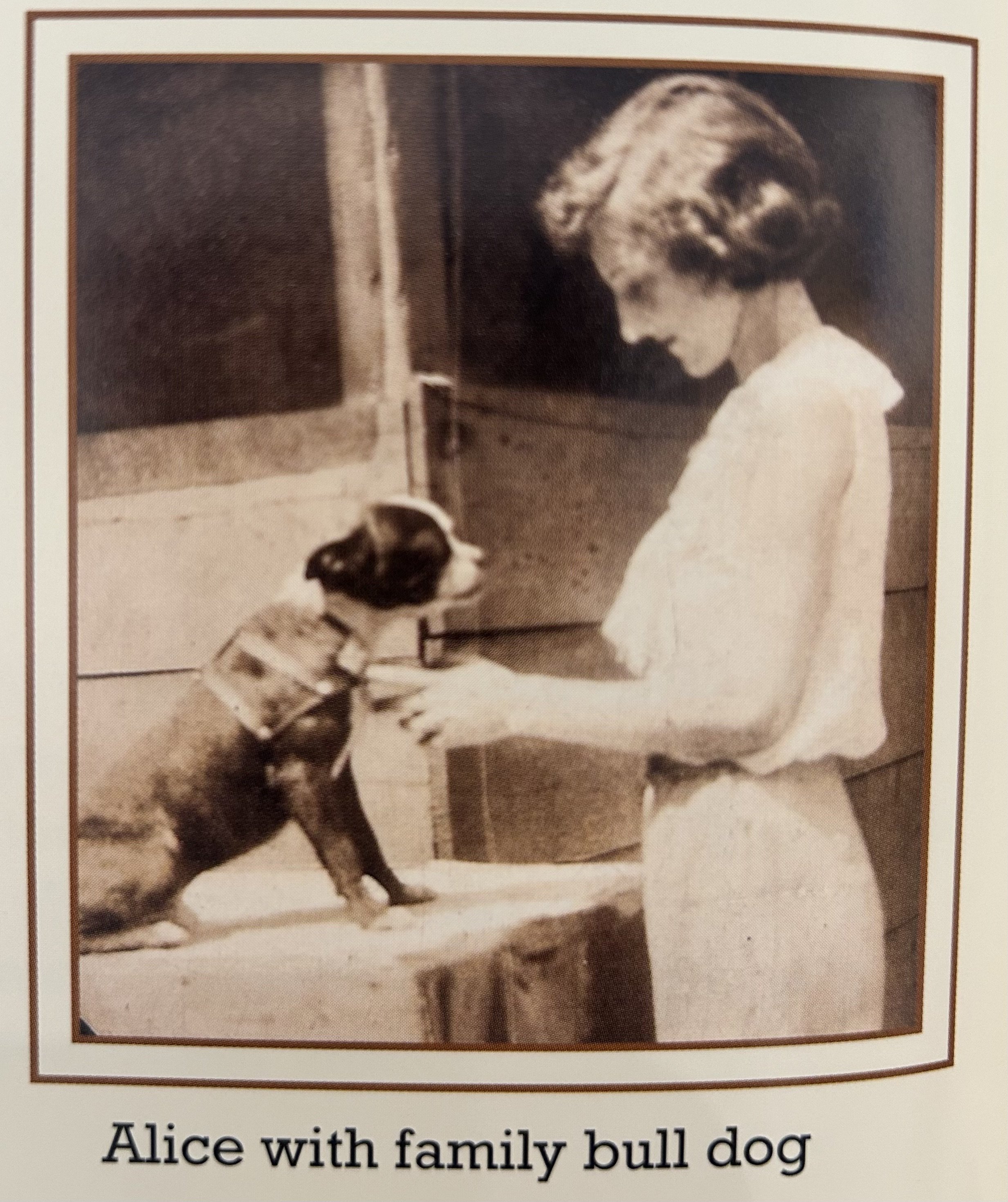 A girl with glasses and short hair sitting on the floor, smiling, with her family dog, a Medium-sized Border Collie, lying next to her.