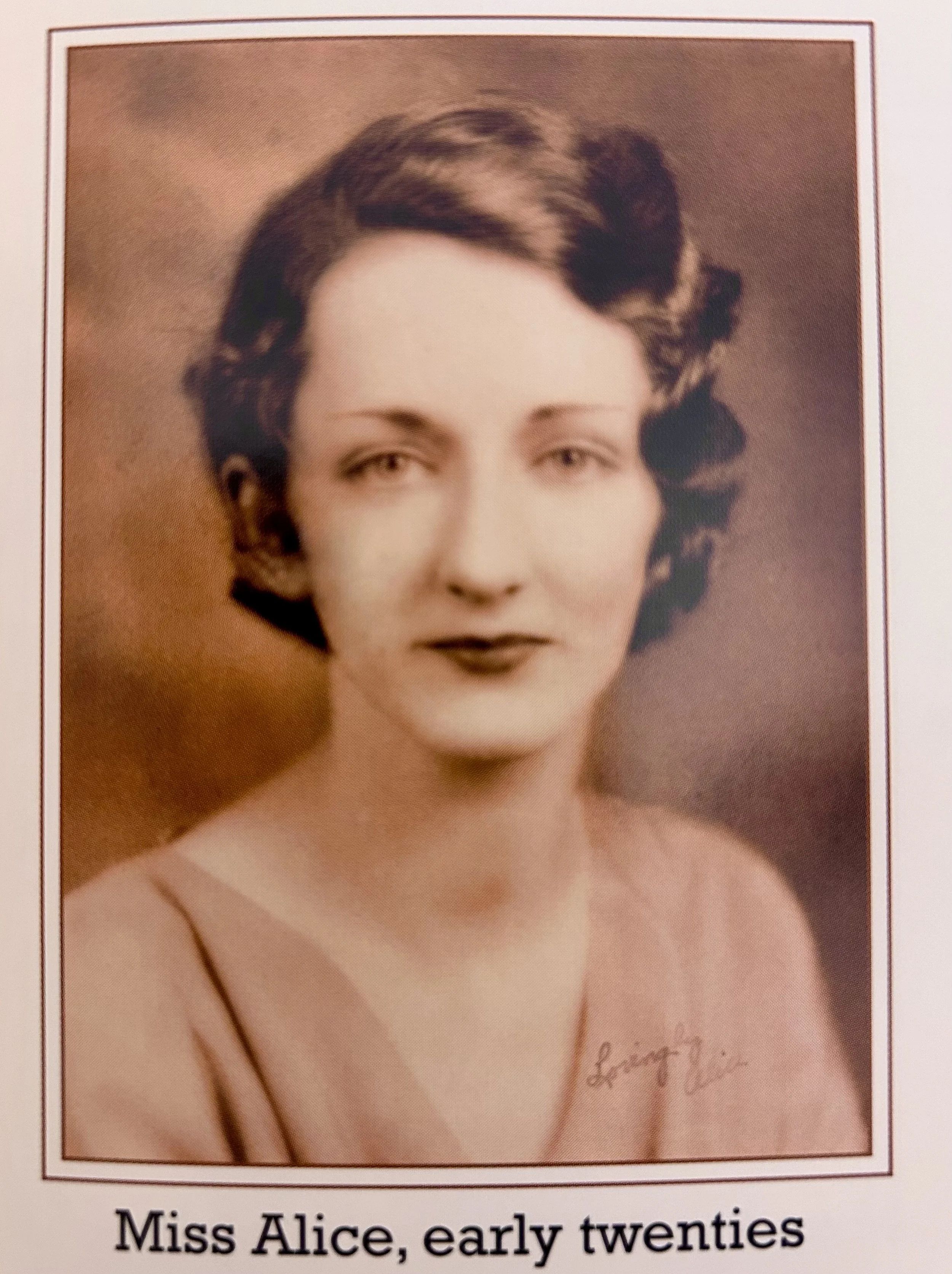 A vintage portrait photograph of Miss Alice in her early twenties, with wavy dark hair and wearing a thin-strapped dress, taken in the early 1920s.