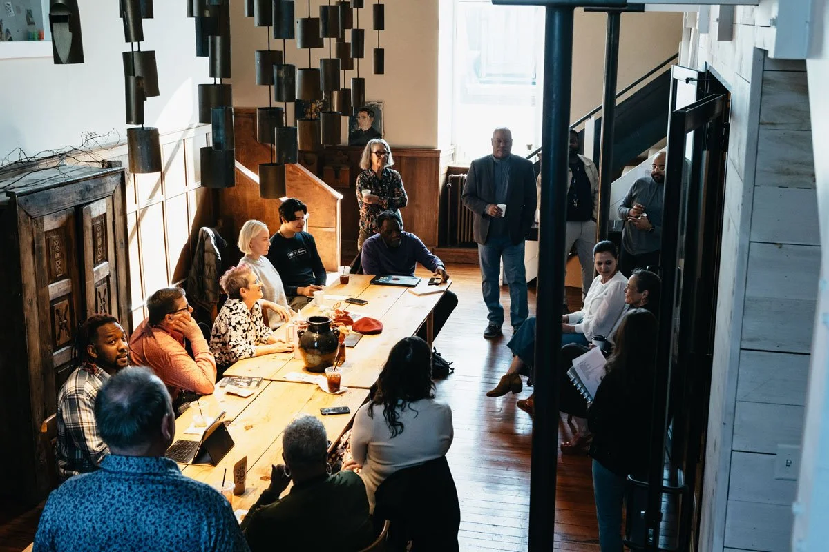 Group of diverse people gathered around a wooden table in a well-lit room, participating in a meeting or discussion in East Falls, Philadelphia.