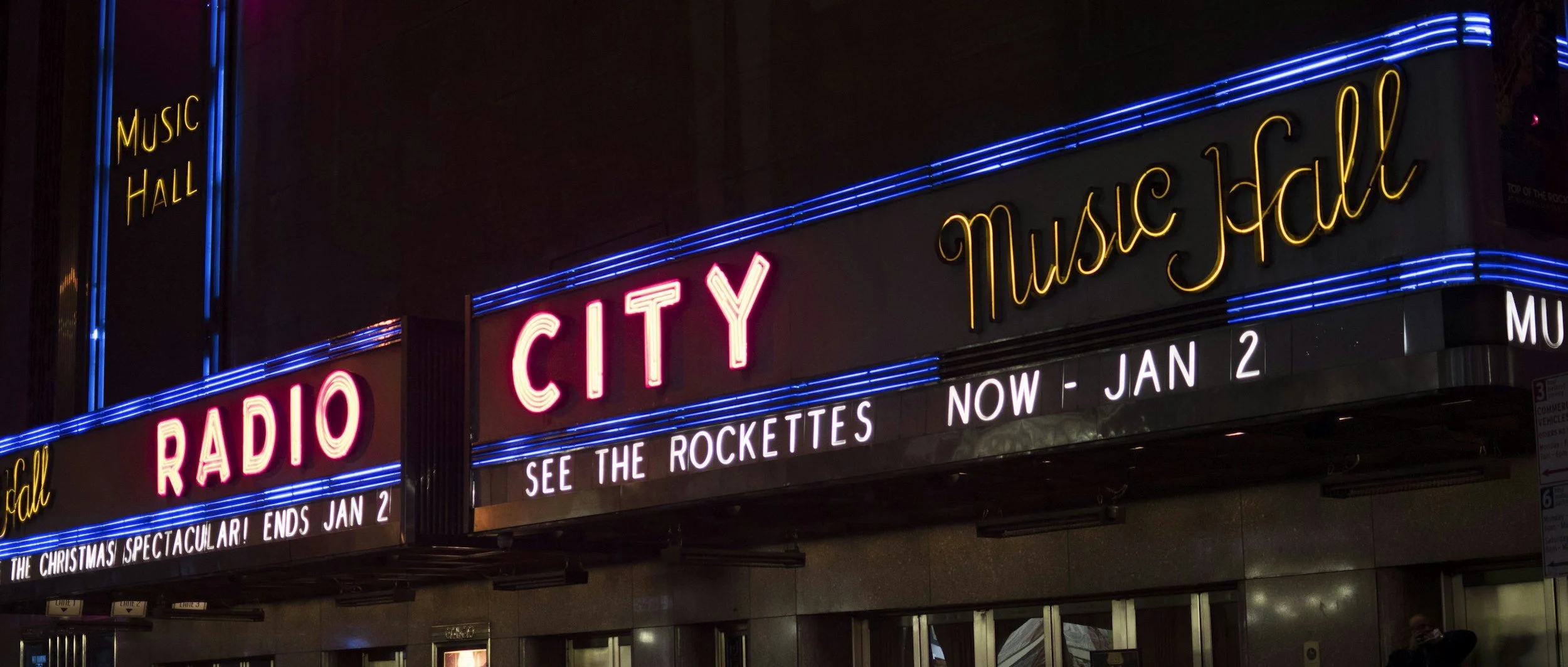 Neon sign for Radio City Music Hall with a marquee displaying upcoming shows and dates.