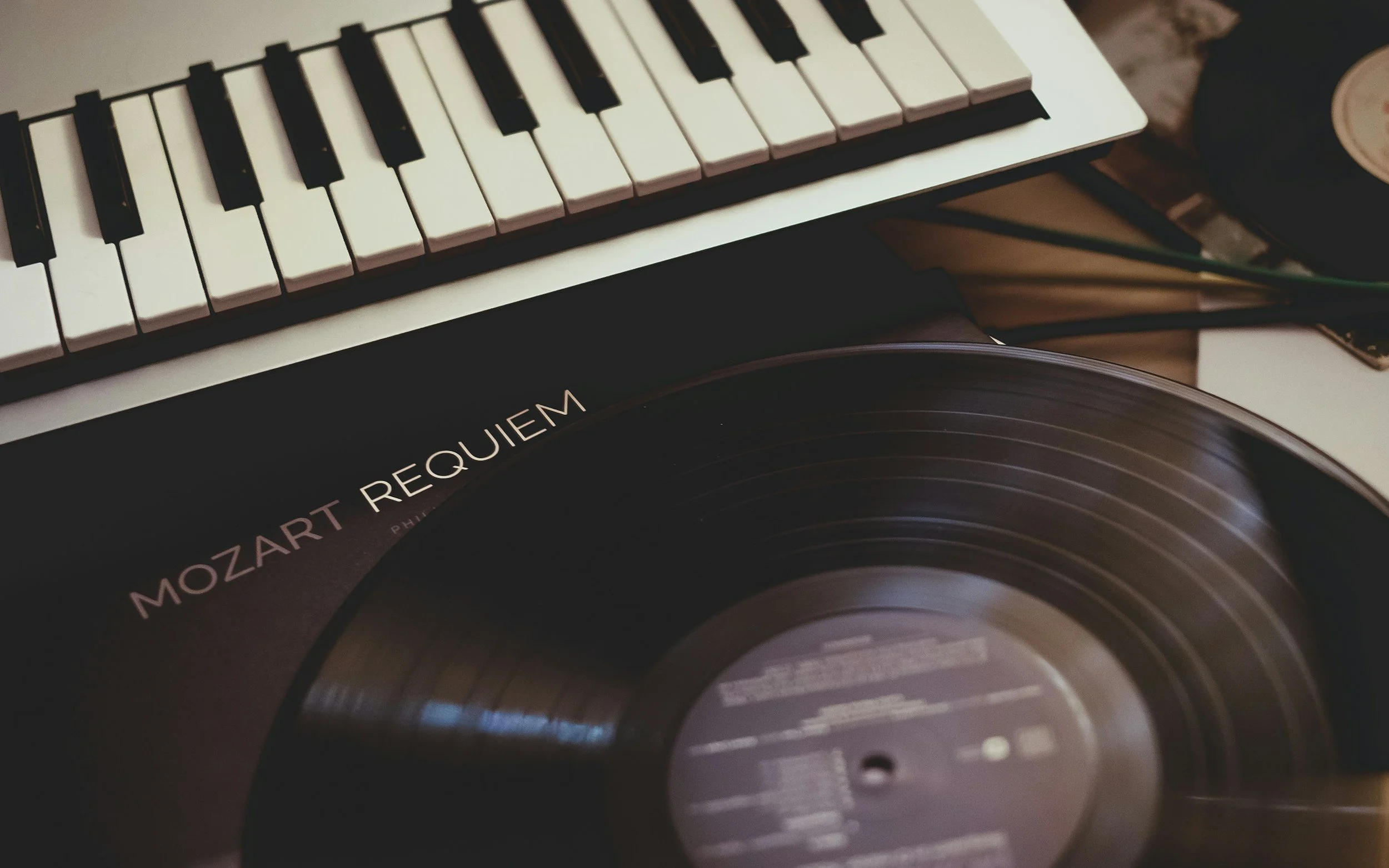 Close-up of a vinyl record with a black label and the word 'MOZART REQUIEM' printed on it, placed underneath a small electronic keyboard with black and white keys.