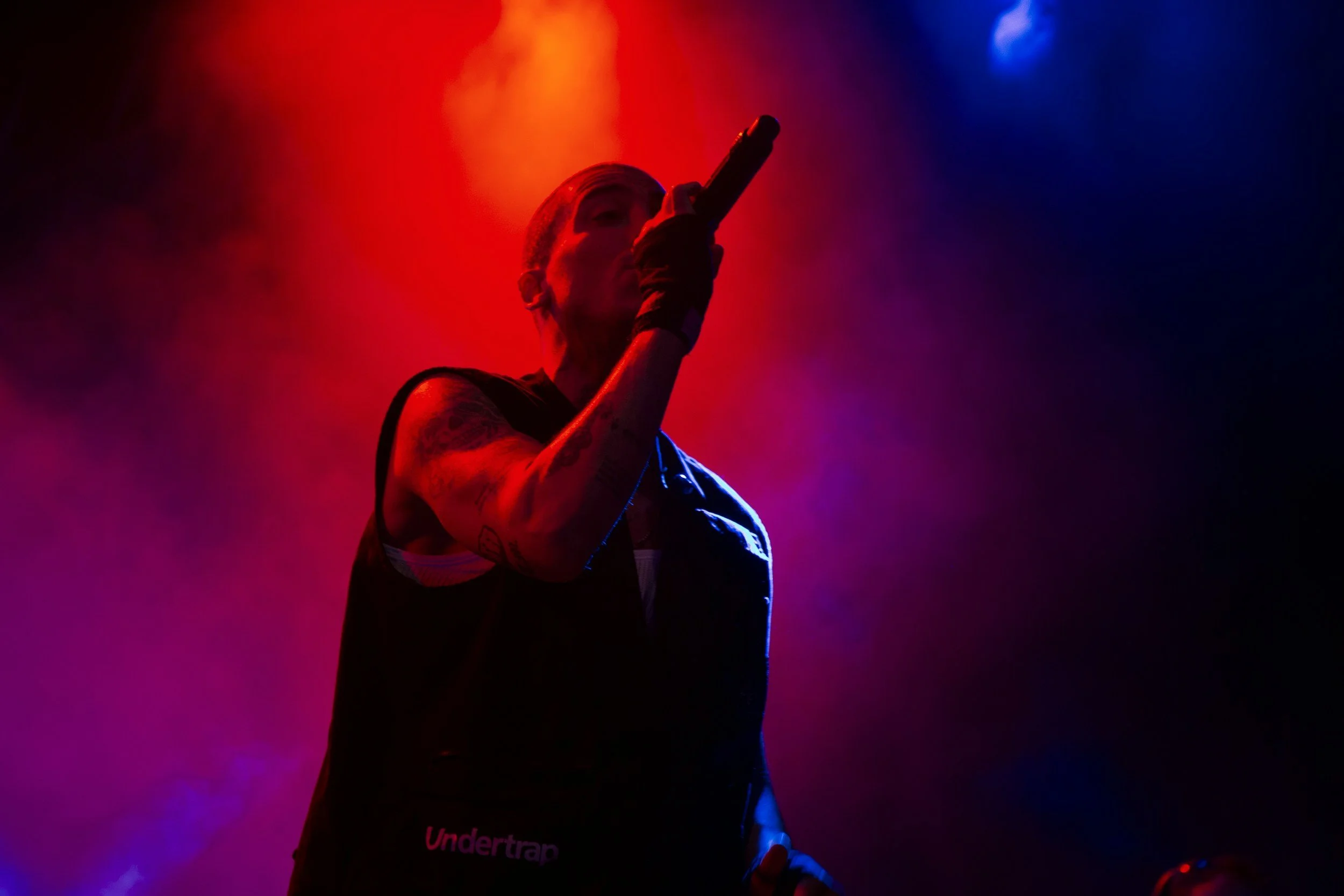 Person performing on stage under colorful lighting with red, purple, and blue hues.