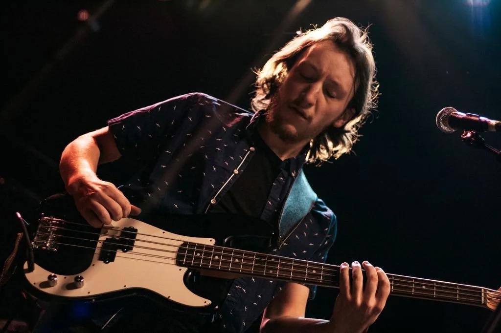 A man with long hair playing an electric guitar on stage, with a microphone nearby.