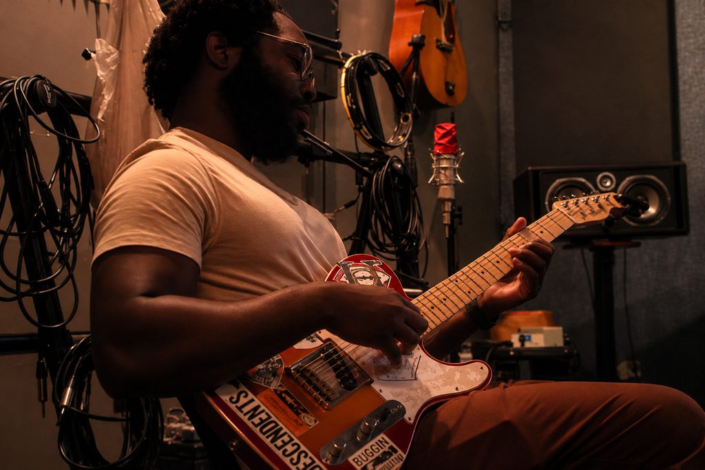 A man playing an electric guitar in a music studio with microphones, speakers, and musical equipment around him.