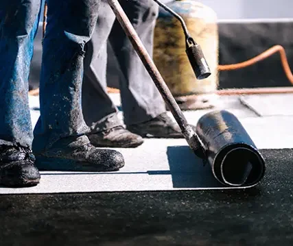 People applying a layer of asphalt on a road with a roller brush.