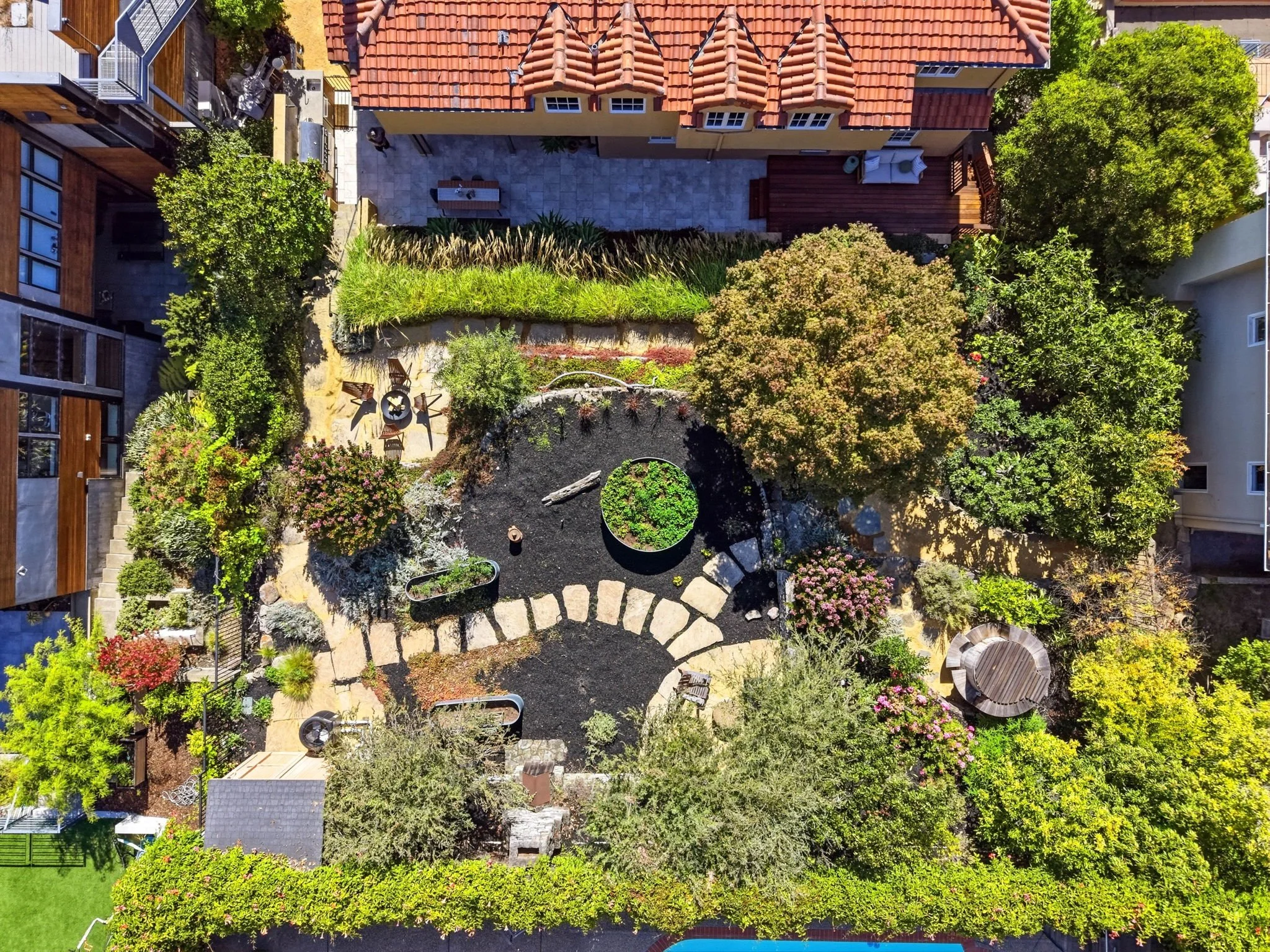An aerial view of a backyard with a patio, lush trees, a garden, and a curved stone pathway.