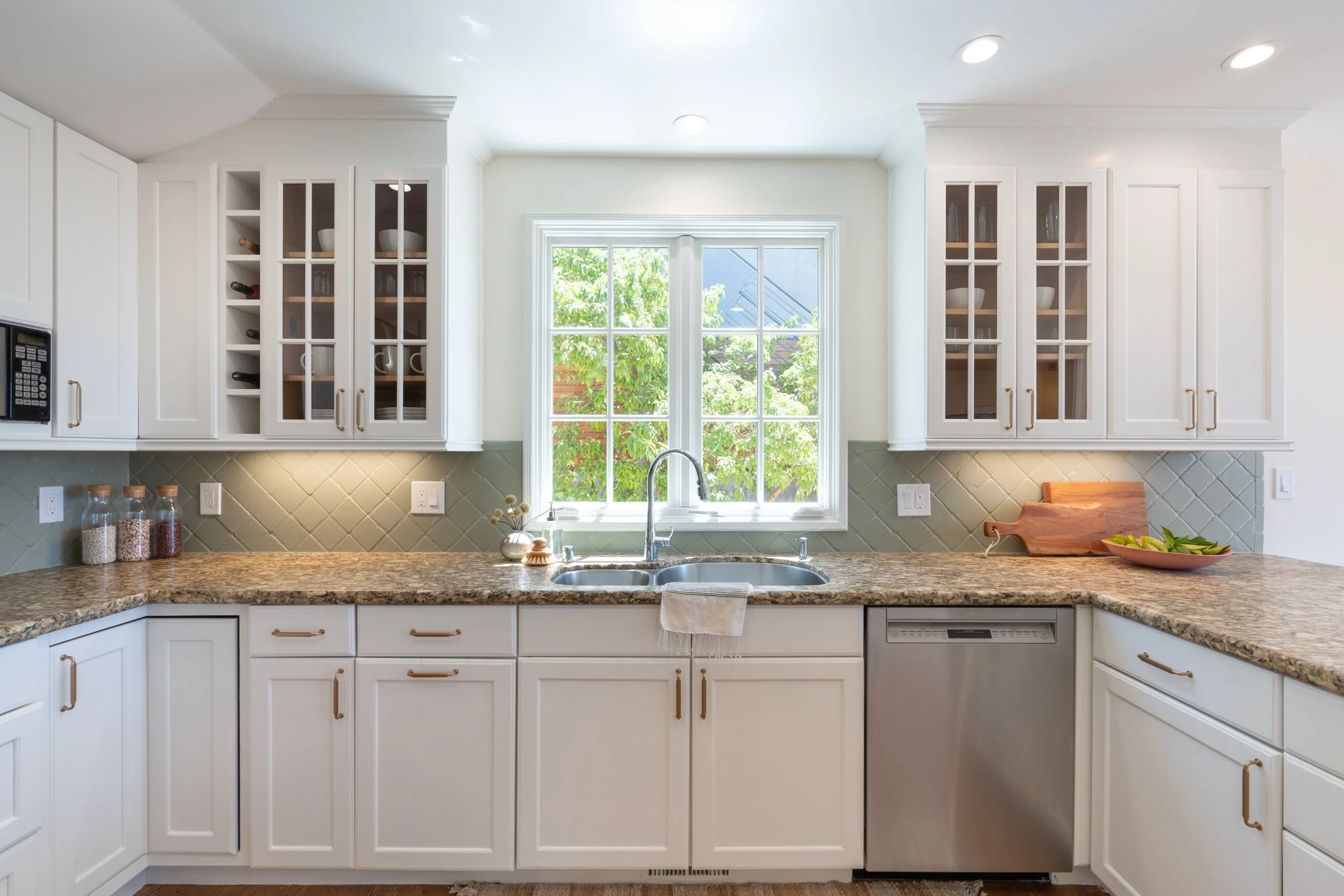 Bright kitchen with white cabinets, granite countertops, window with green trees outside, and under-shelf lighting.