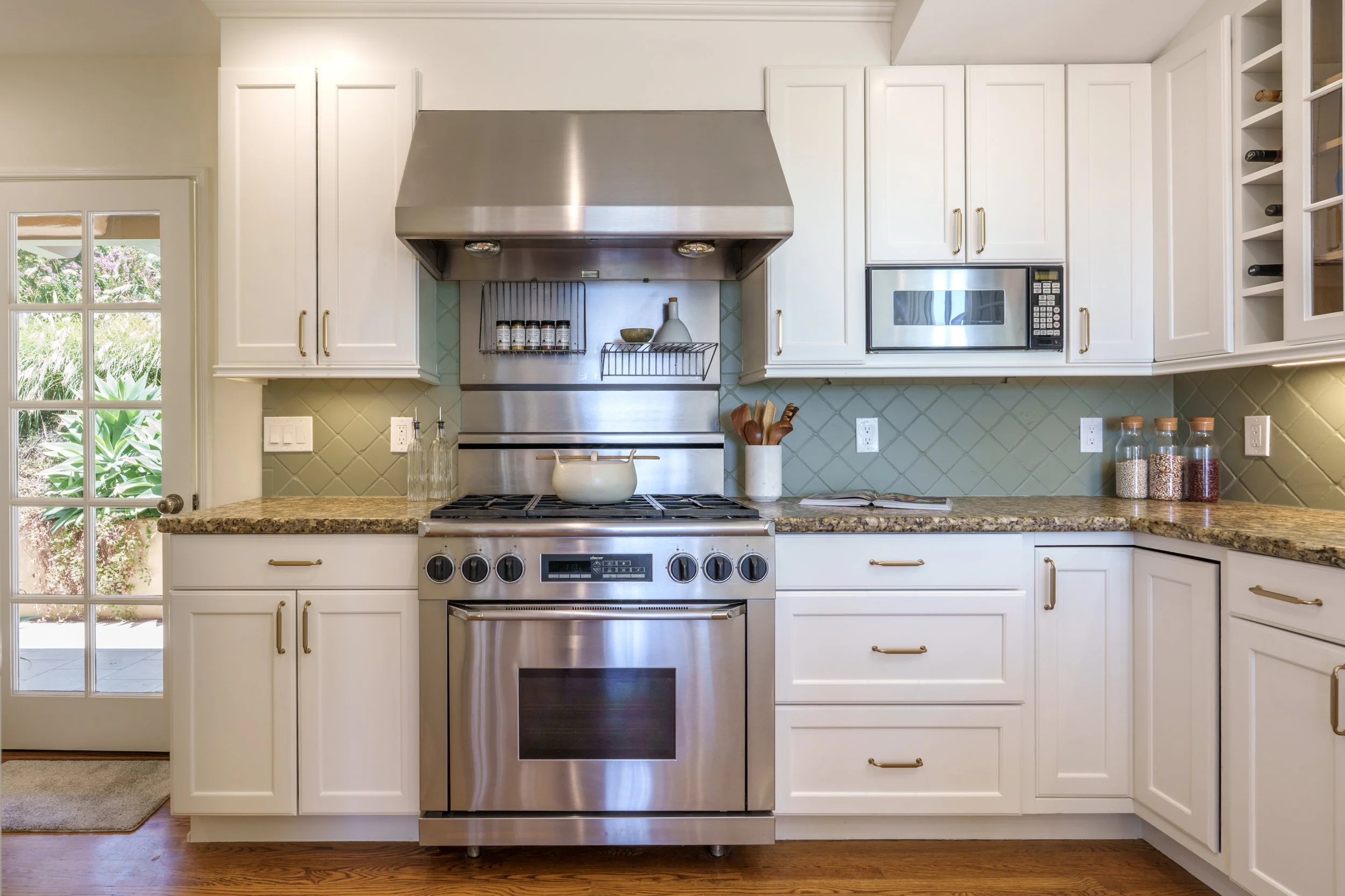 Kitchen with white cabinets, stainless steel oven and microwave, granite countertop, and a windowed door leading outside. There are kitchen utensils and spice jars on the counter.