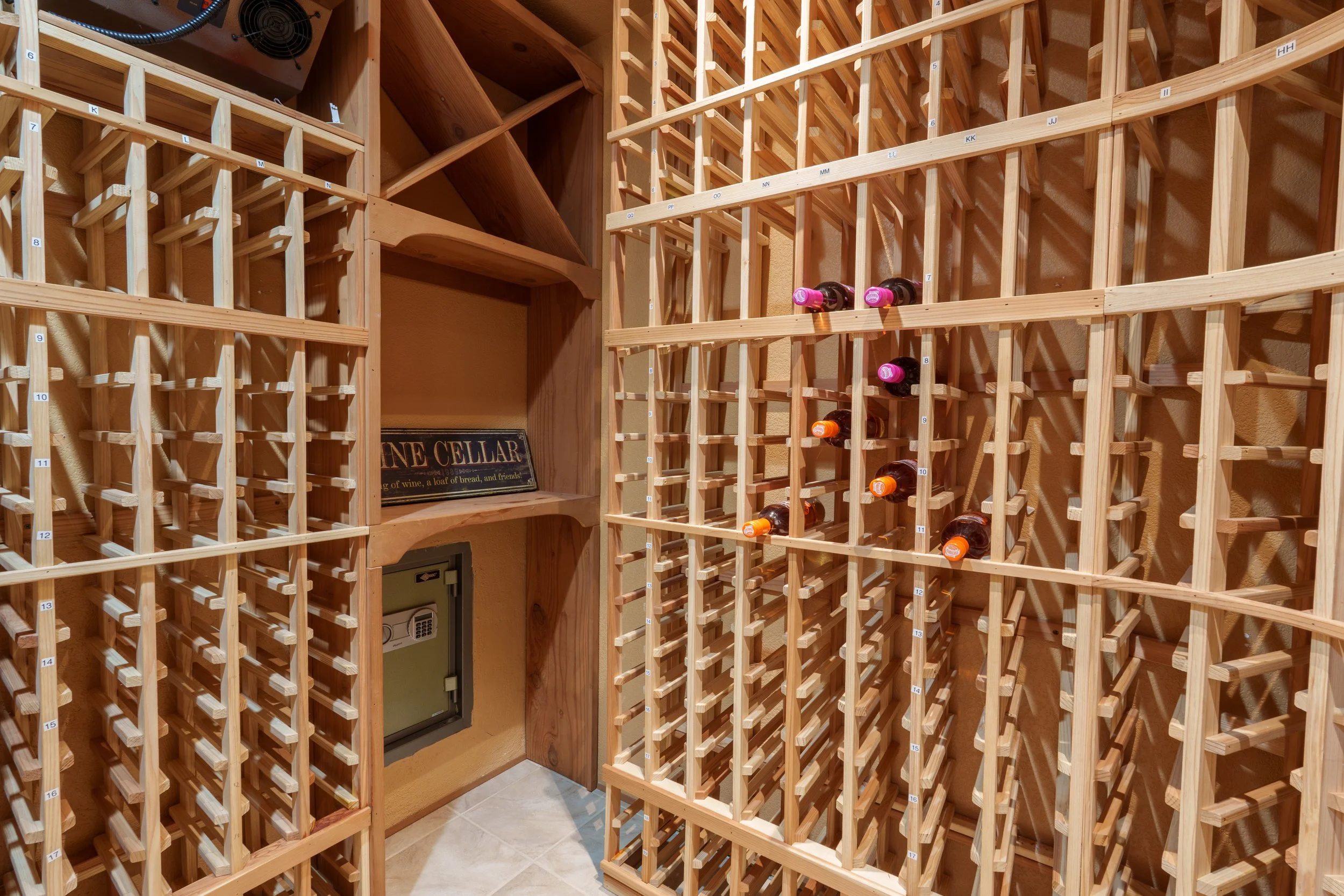 A wine cellar with multiple wooden wine racks, some holding bottles with pink and orange caps, and a sign that reads "WINE CELLAR".