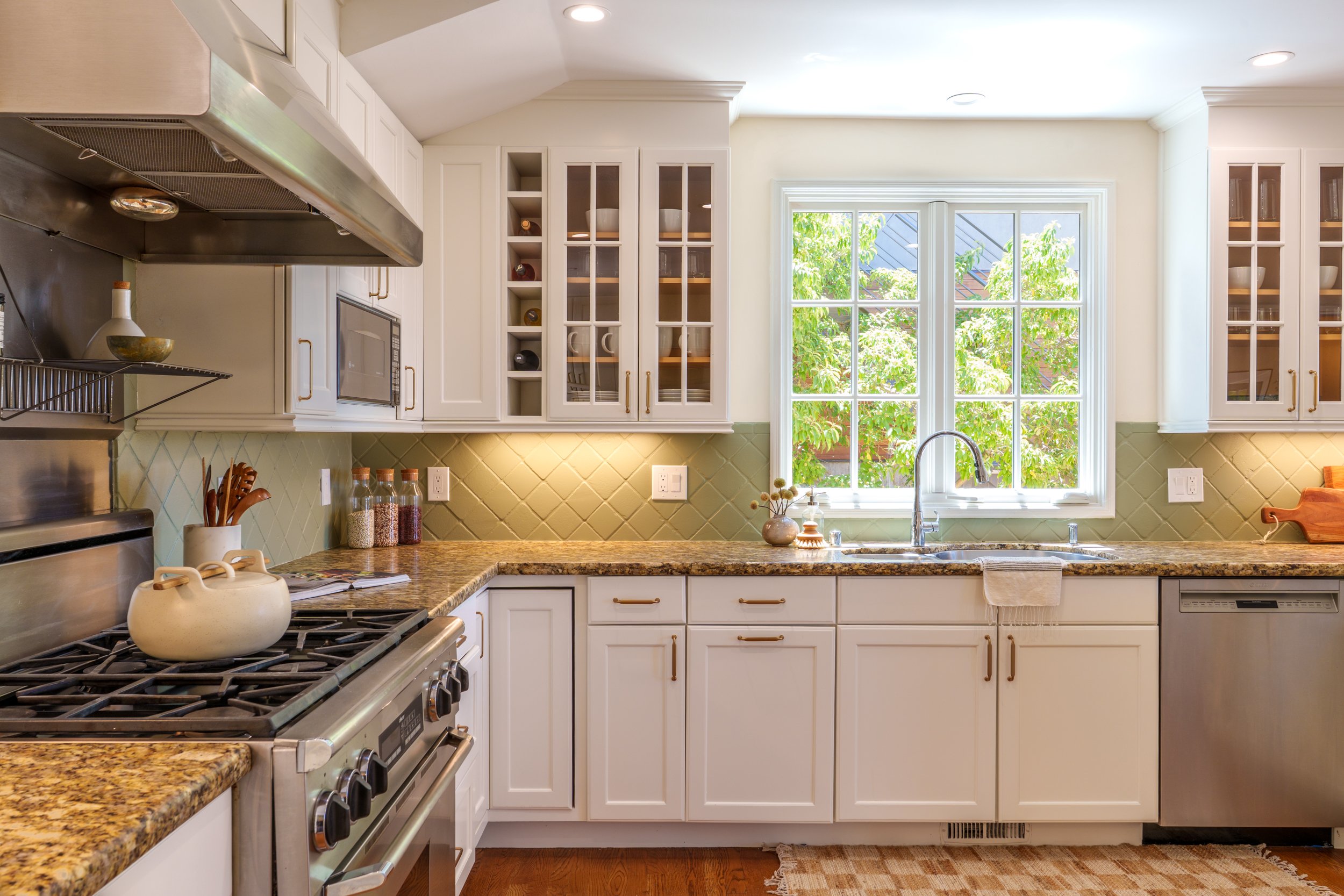 Kitchen with white cabinets, granite countertop, and a large window with greenery outside.