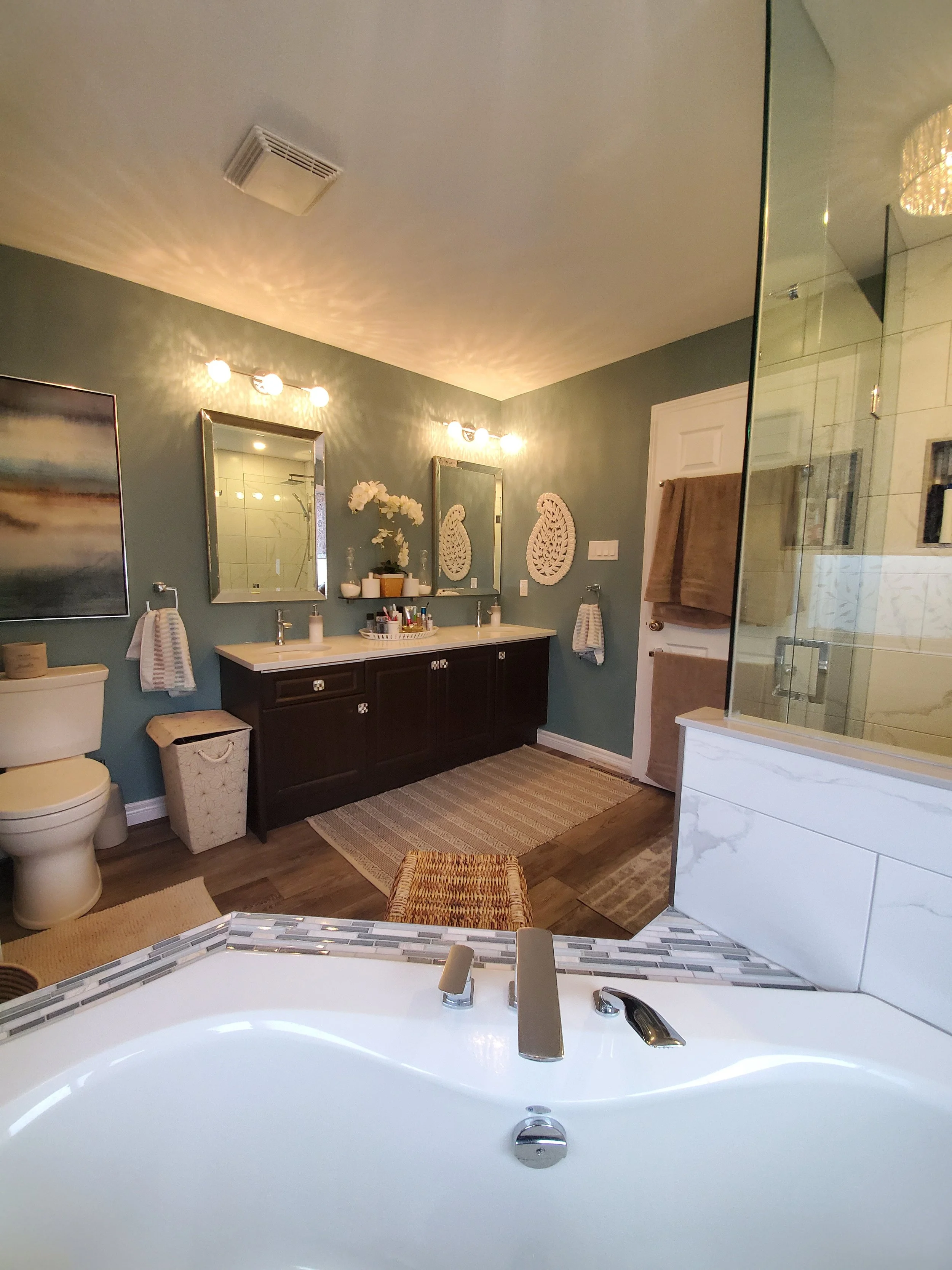 Bathroom with dual sinks, mirrors, decorative wall art, towels, and a bathtub with a modern faucet.