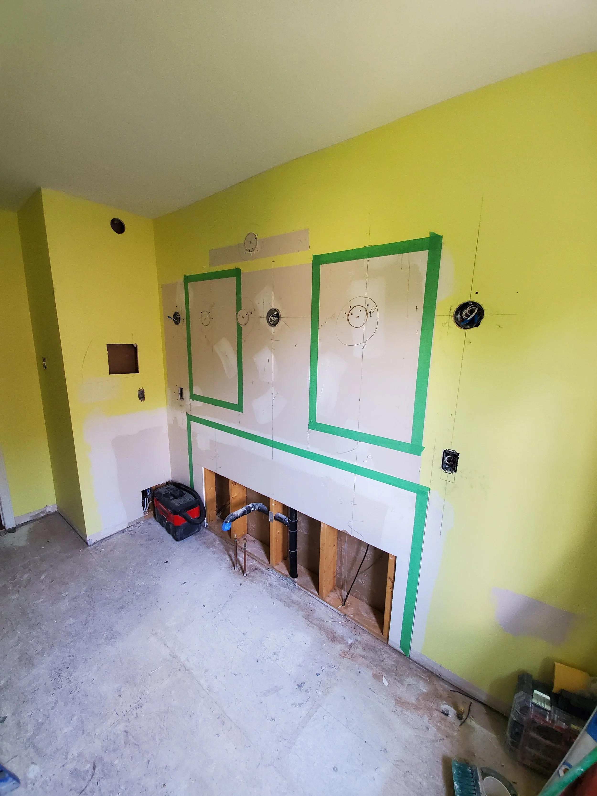 Kitchen under renovation with bright yellow walls, electrical wiring, outlets, and a partially built cabinet or counter with exposed wood framing, and construction tools on the floor.