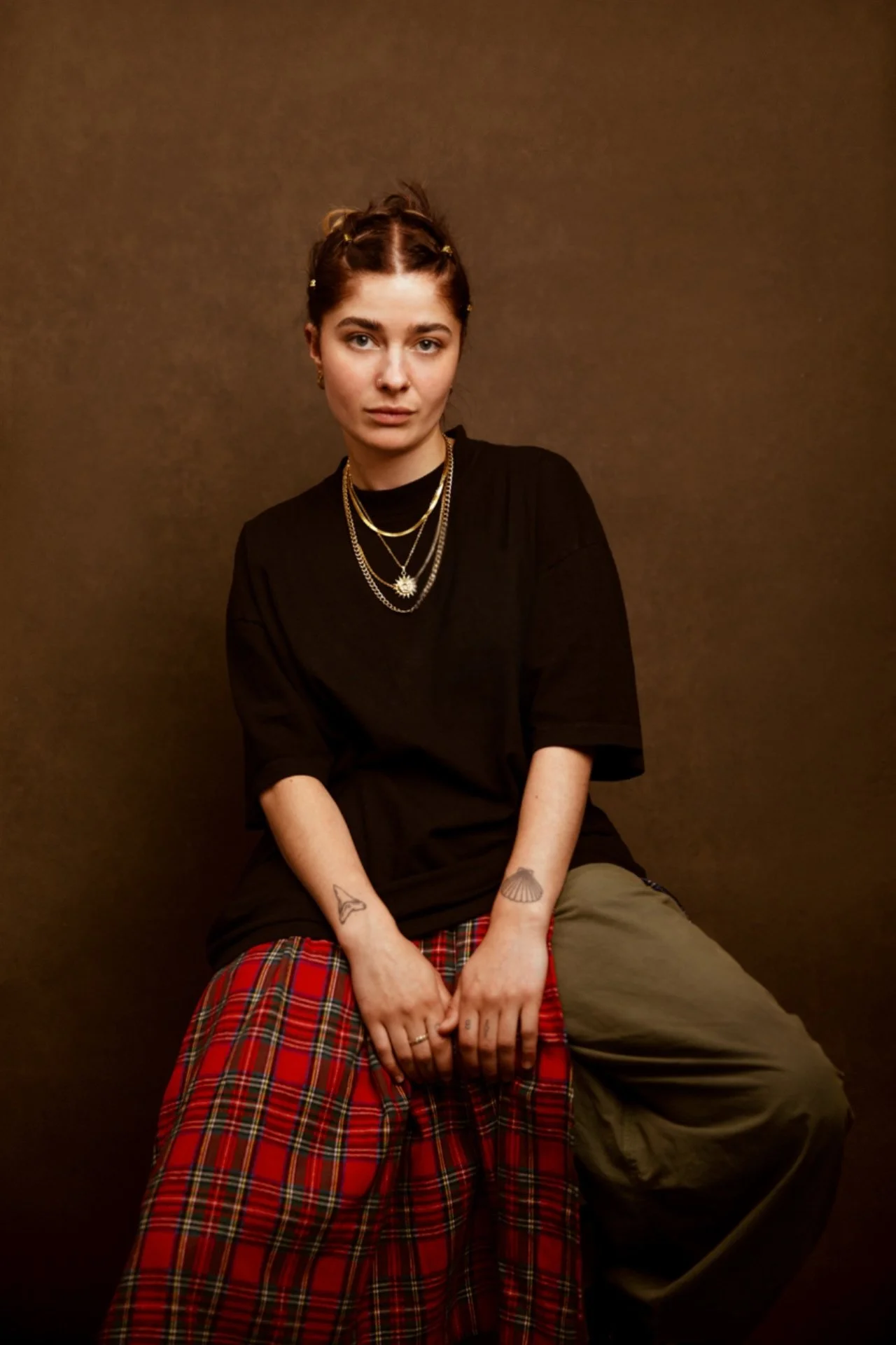 Reena Wright actor headshot sitting on a stool with gold chains black t shirt and tarten skirt