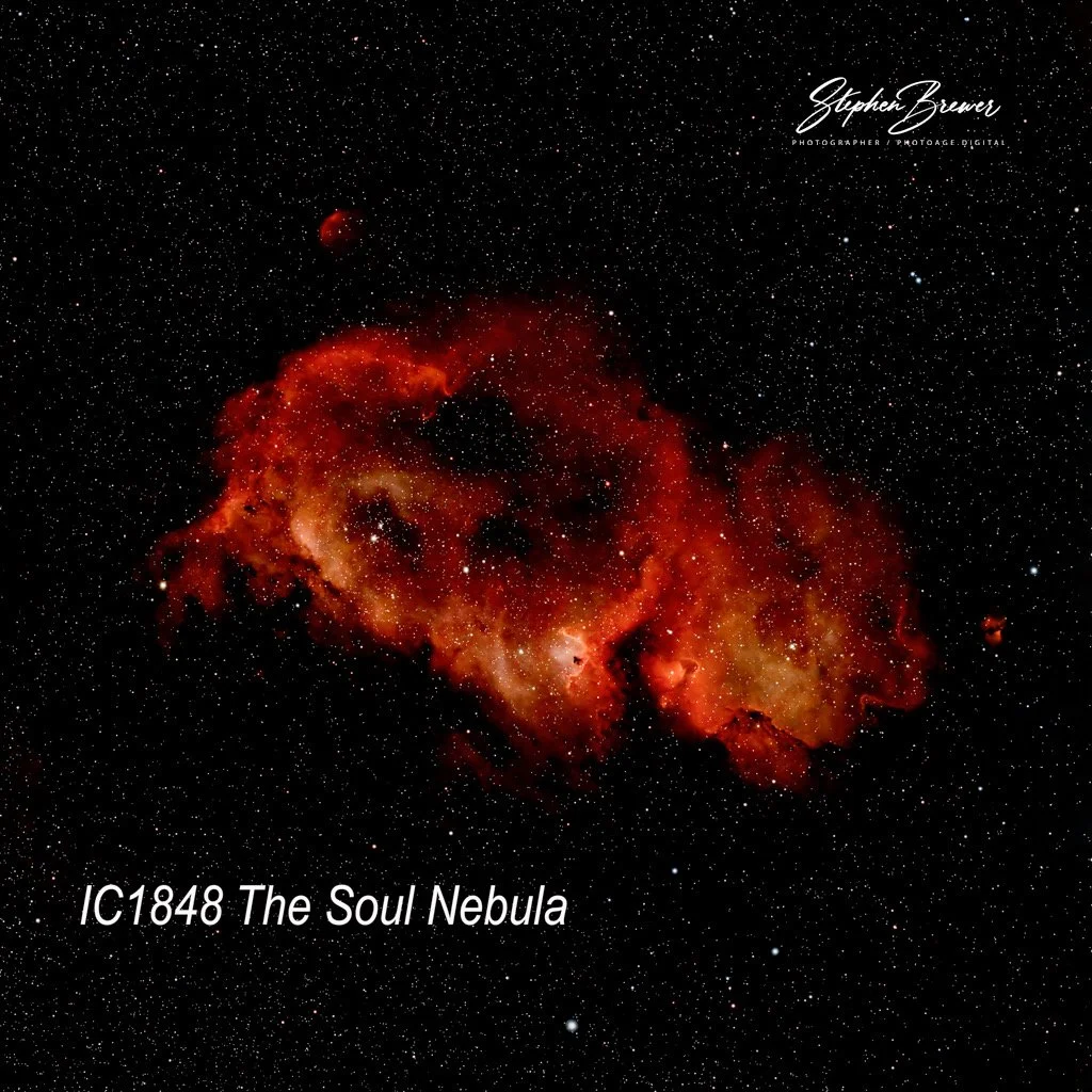 A photograph of the IC 1848 The Soul Nebula, showing a large, red, glowing nebula with surrounding stars in space.