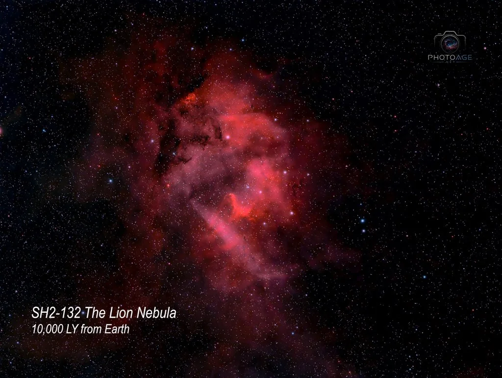 Photo of the Lion Nebula, a red and pink gaseous nebula in space, with numerous stars scattered throughout the background. Text overlays indicate it is the SH2-132 The Lion Nebula, located 10,000 light-years from Earth.