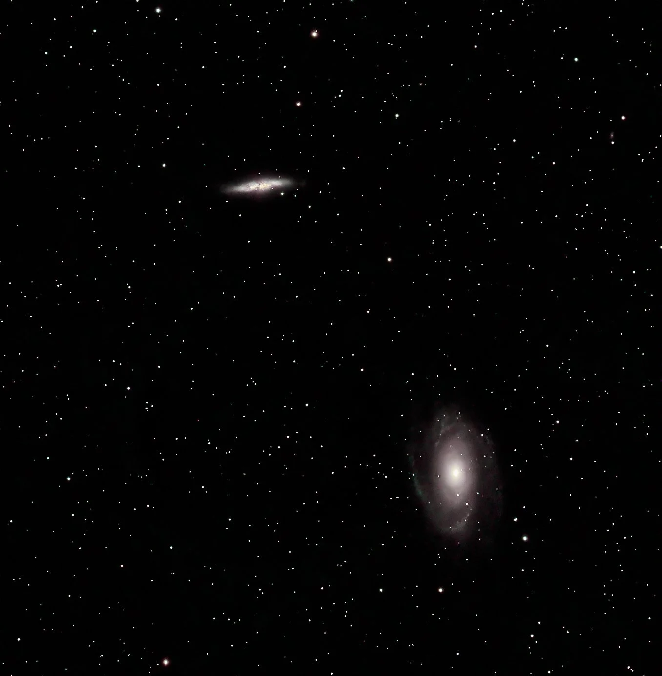 A wide view of outer space showing numerous stars, with two visible galaxies, one towards the bottom right and another towards the center left.