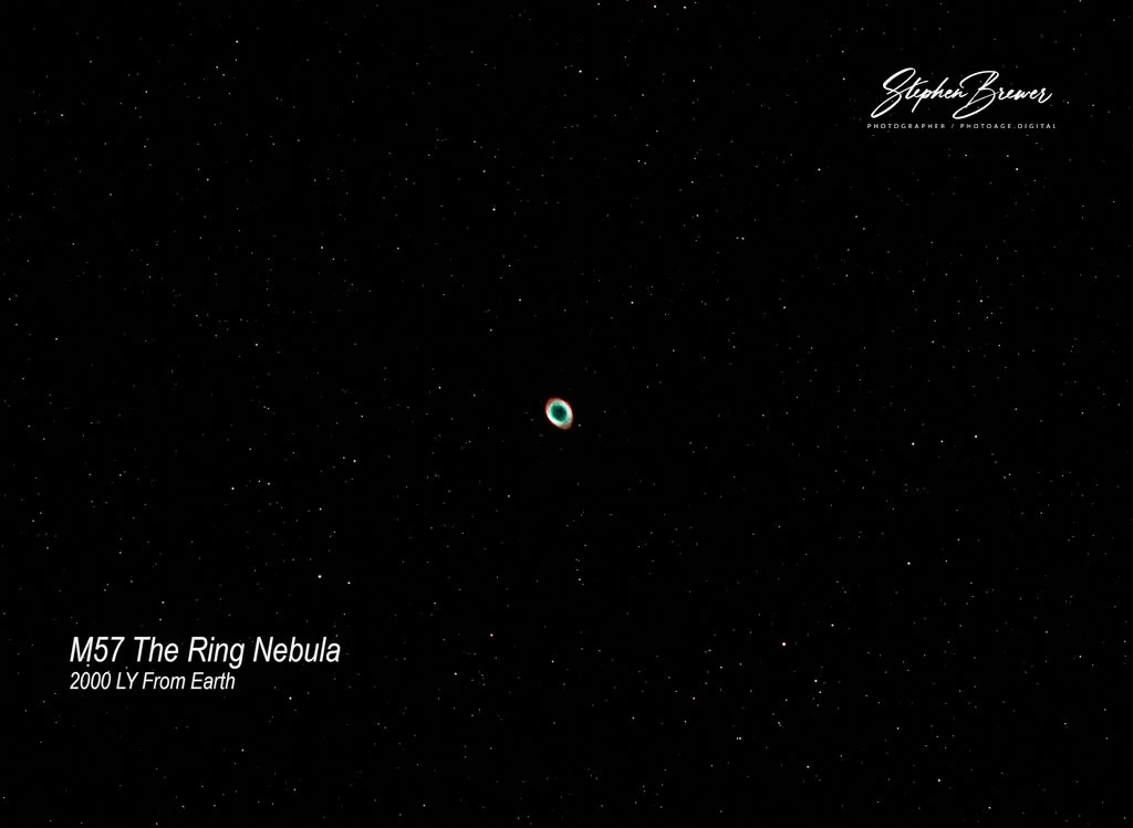 A photograph of the night sky showing the Ring Nebula (M57) with numerous stars, taken from Earth, attributed to photographer Stephen Brewer.