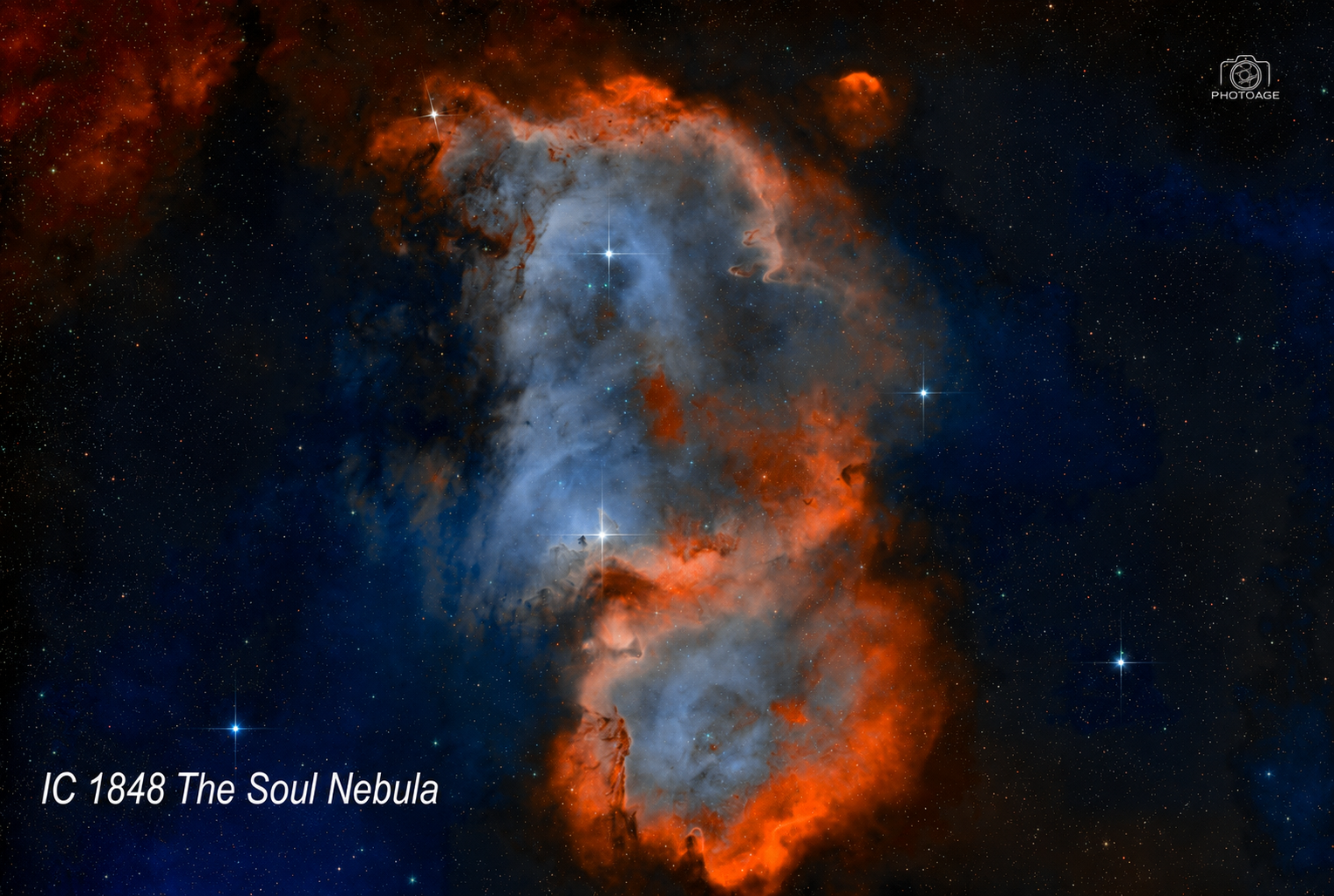 Image of the IC 1848 The Soul Nebula, showing vibrant red, orange, blue, and black clouds of gas and dust with bright stars scattered throughout.