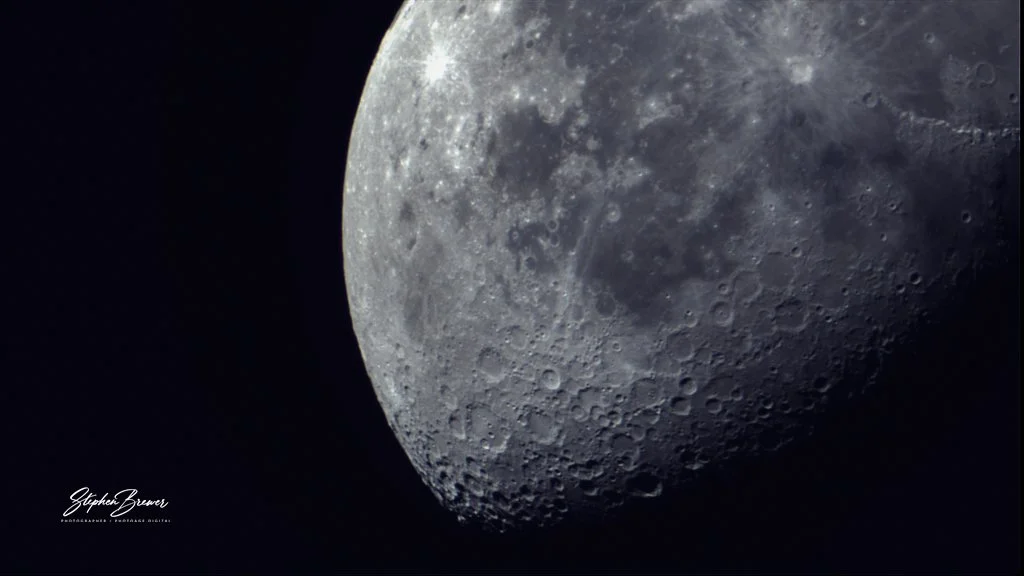 Close-up photograph of the moon's cratered surface with a dark background.