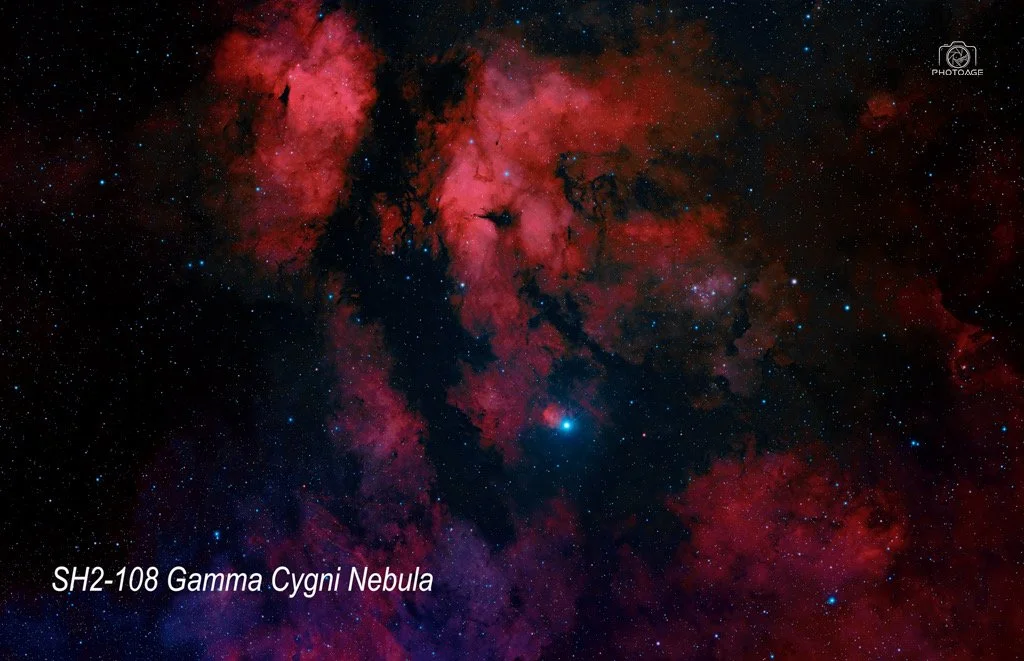 A deep space photograph of the Gamma Cygni Nebula, with red and pink clouds of gas and dust, stars scattered across the background, and text labels indicating "SH2-108 Gamma Cygni Nebula."