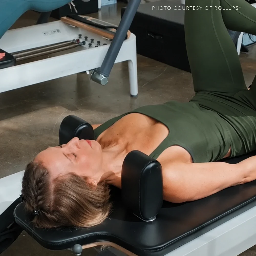 A woman lying on her back on a medical or therapy table, with her eyes closed, receiving a treatment using specialized equipment for her neck and head area. The scene appears to be in a clinical or wellness setting.