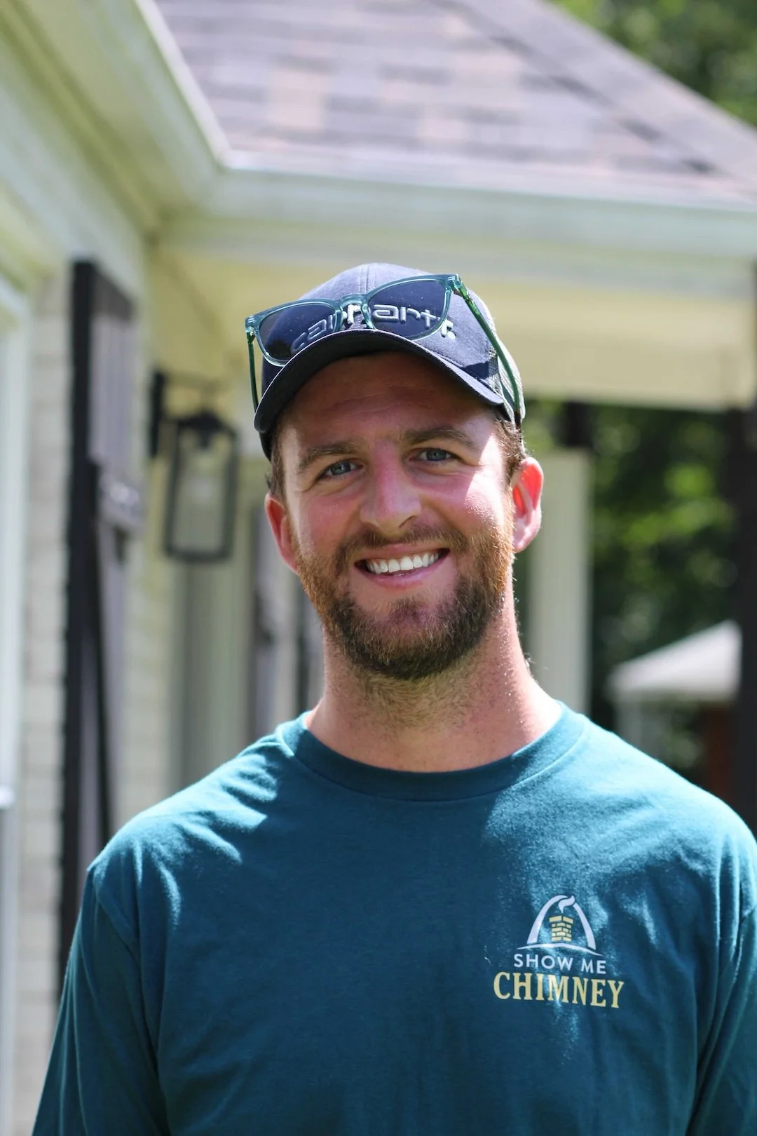 Jake Goldson from Show Me Chimney, formerly Safe Sweep, stands outiside a home wearing a SHow Me Chimney shirt.