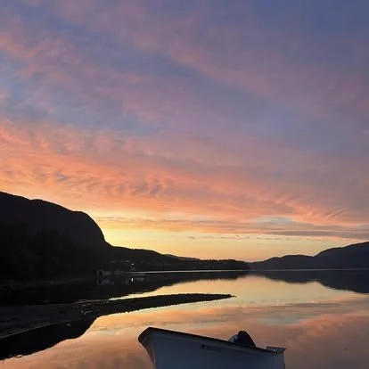 Sunset over a lake with colorful clouds and mountain silhouettes in the background, with a boat in the foreground.
