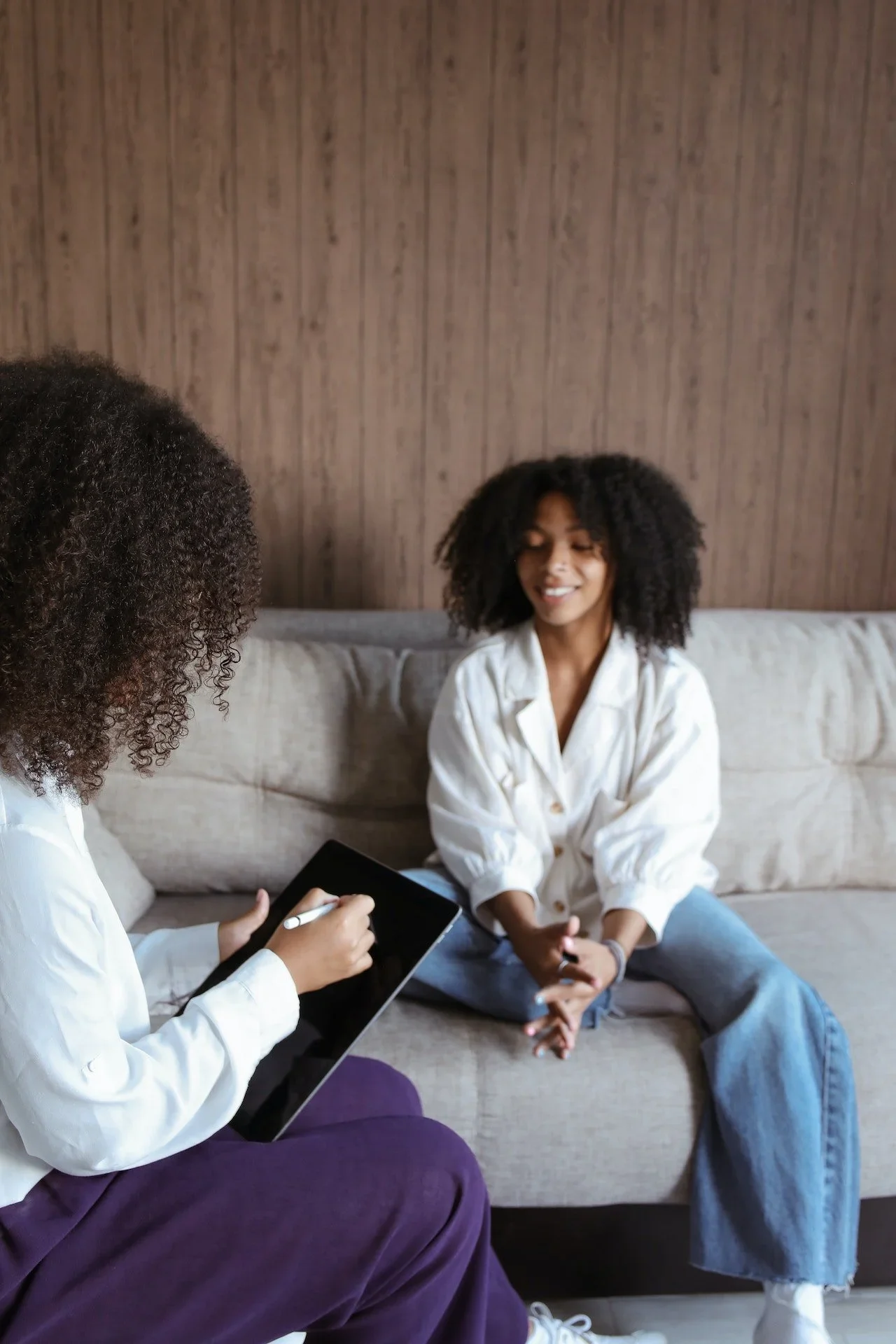 A woman with curly hair smiling while talking to another woman holding a tablet with a stylus.