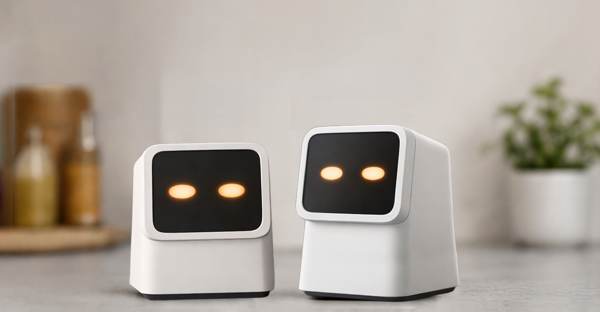Two white, robot-like devices with black screens displaying two glowing orange eyes, placed on a light-colored surface in a minimalist indoor setting.