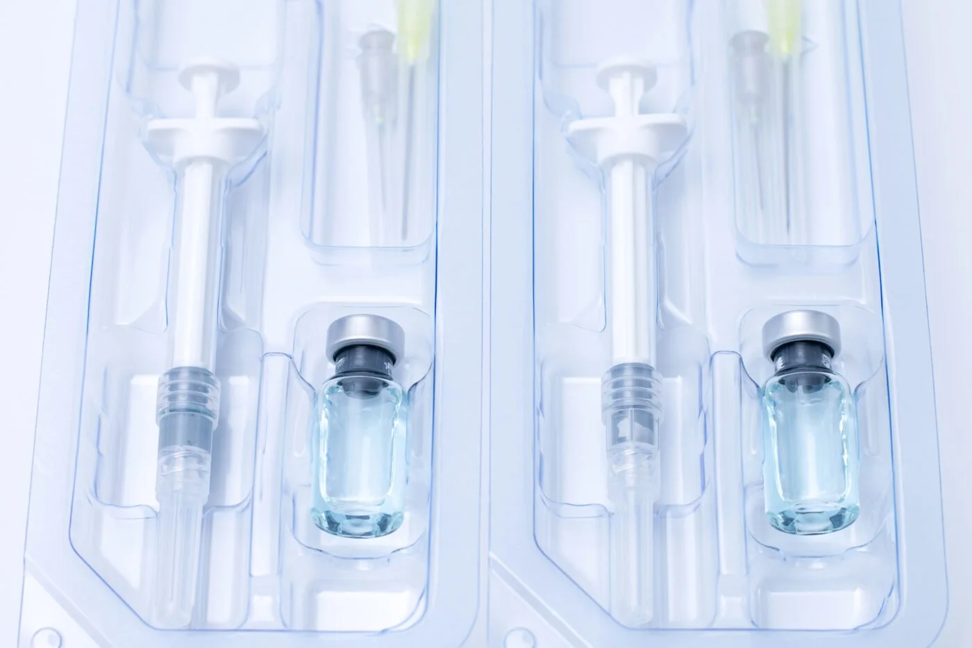 Two glass vials filled with a clear liquid, mounted in a medical tray with embedded syringes and injector system.
