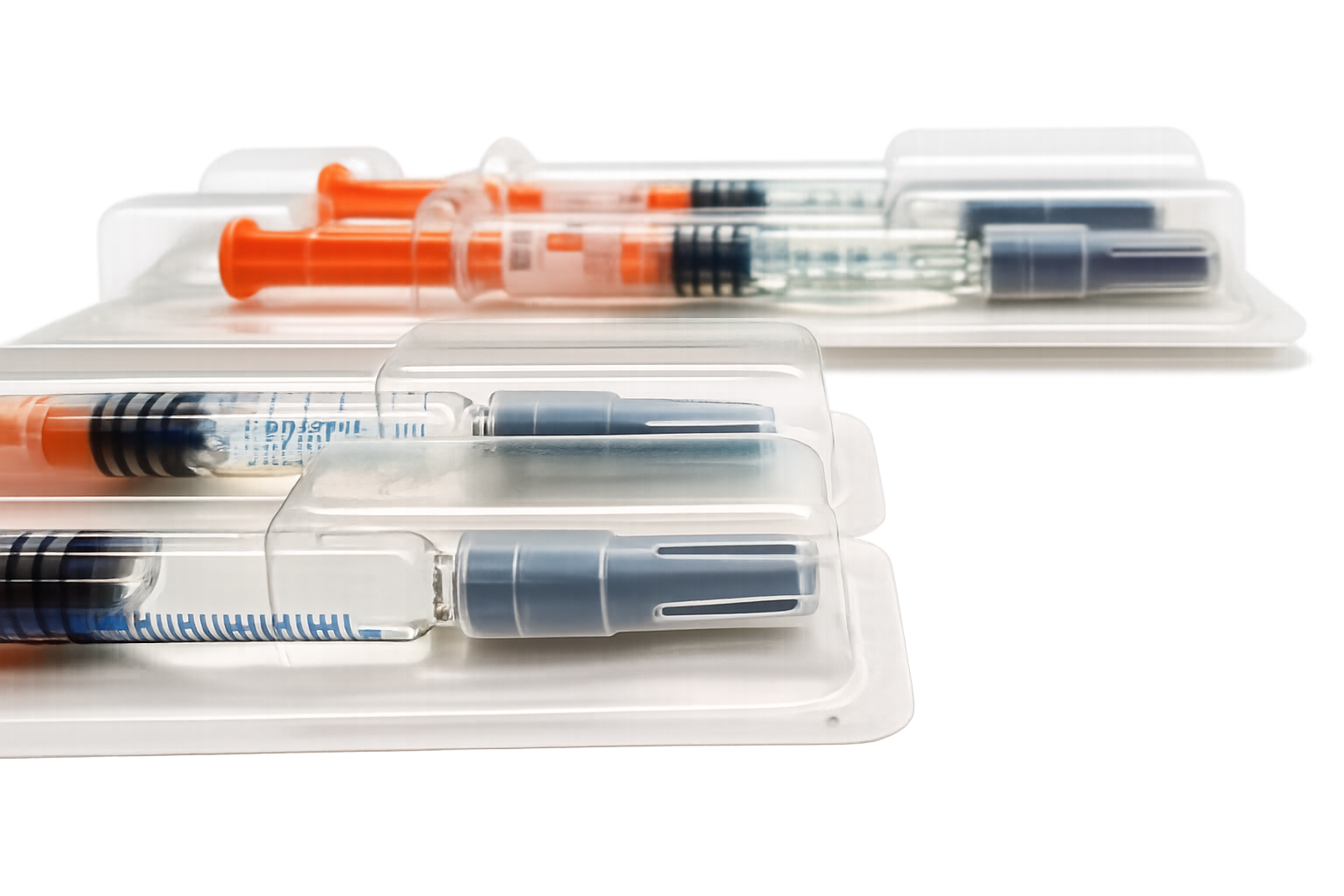Multiple syringes filled with liquid in clear plastic trays, with some syringes capped and some with needles covered, arranged on white surfaces.