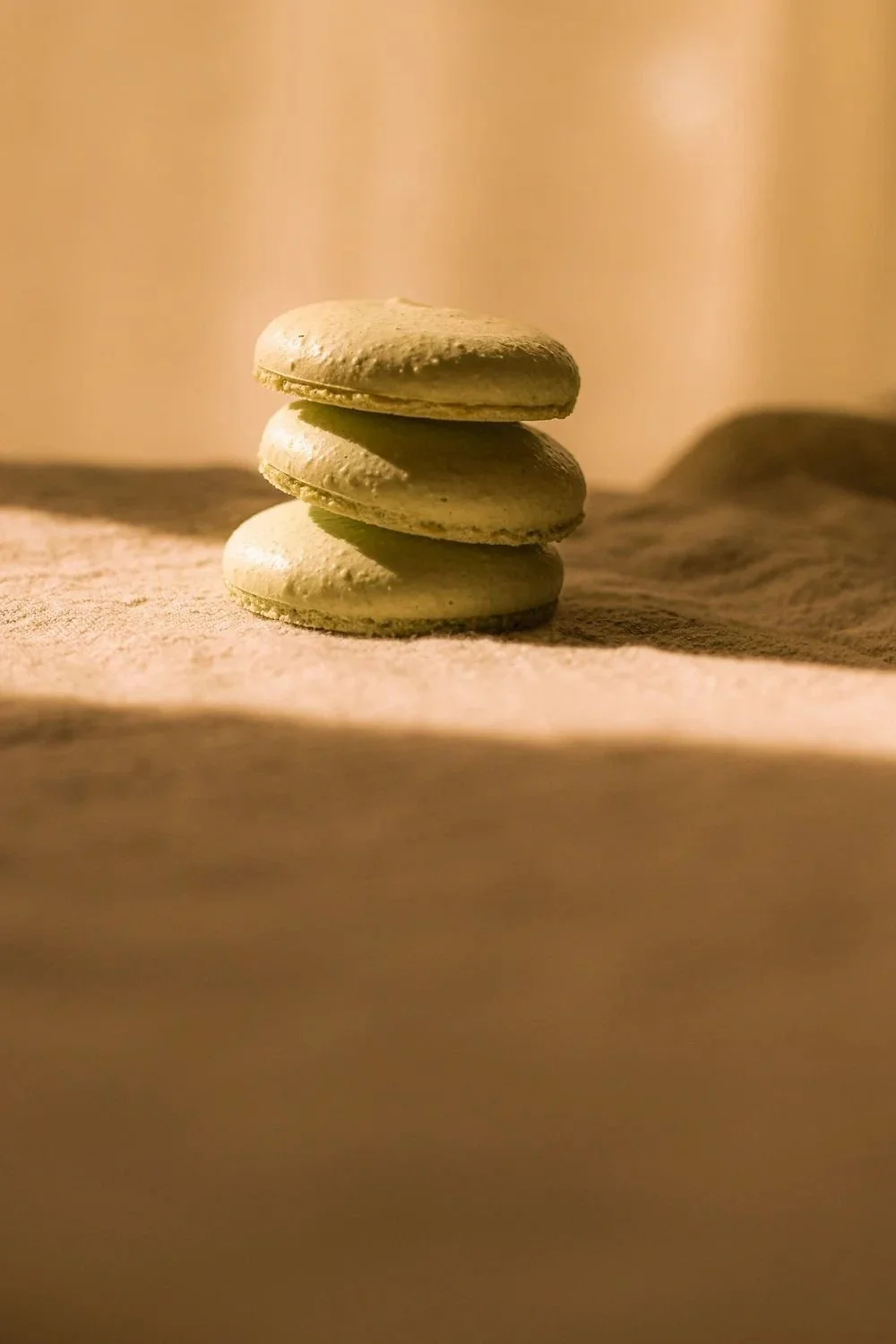 Three macarons stacked on a rustic wooden surface, with a warm and soft lighting background.