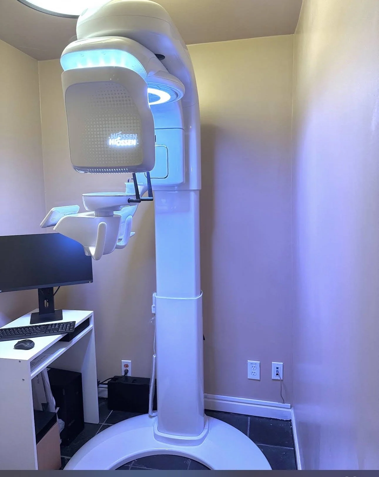 A dental cone beam CT scanner in a room with a computer and monitor.