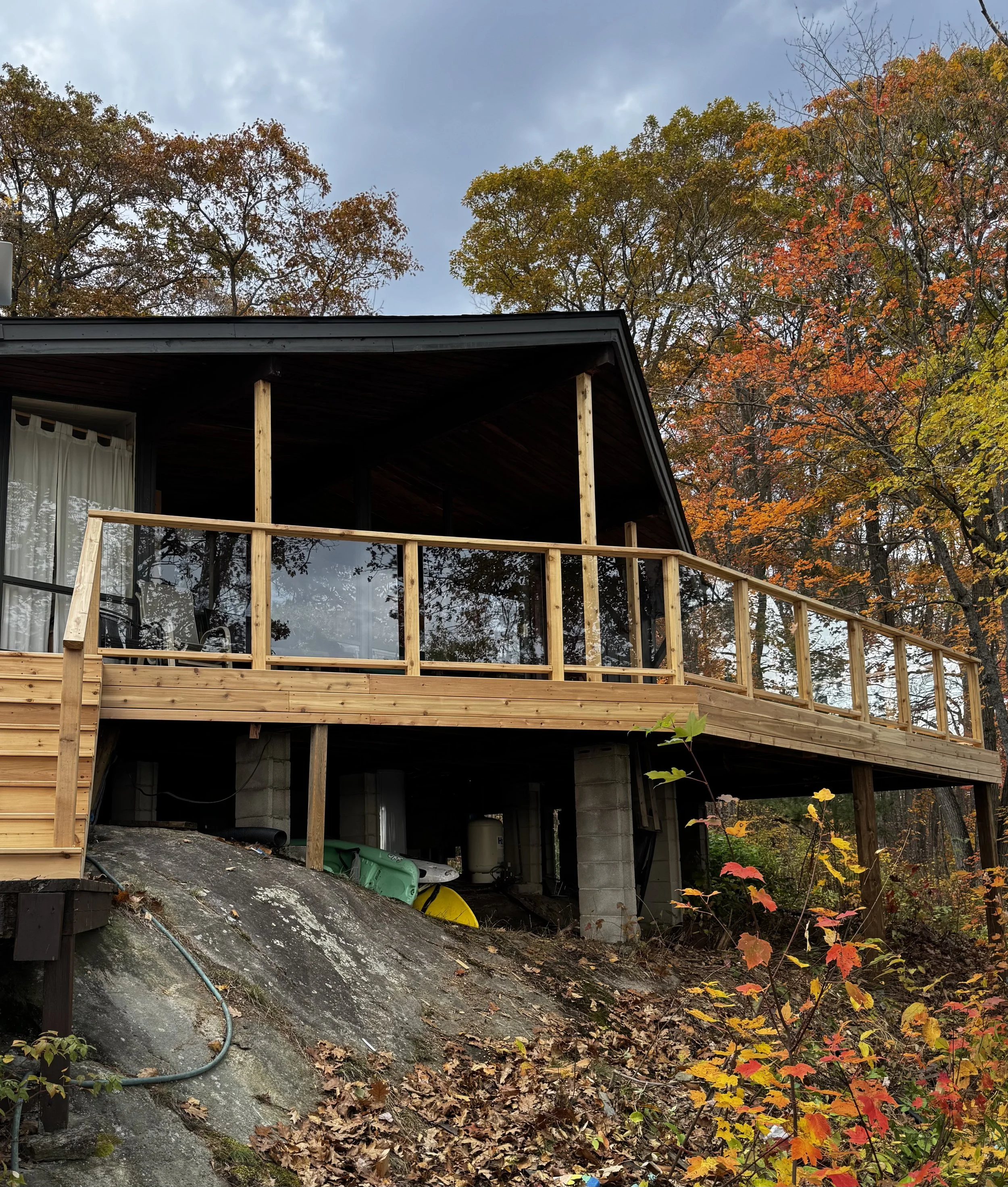 A house under construction on a sloped land with trees showing autumn colors in the background.