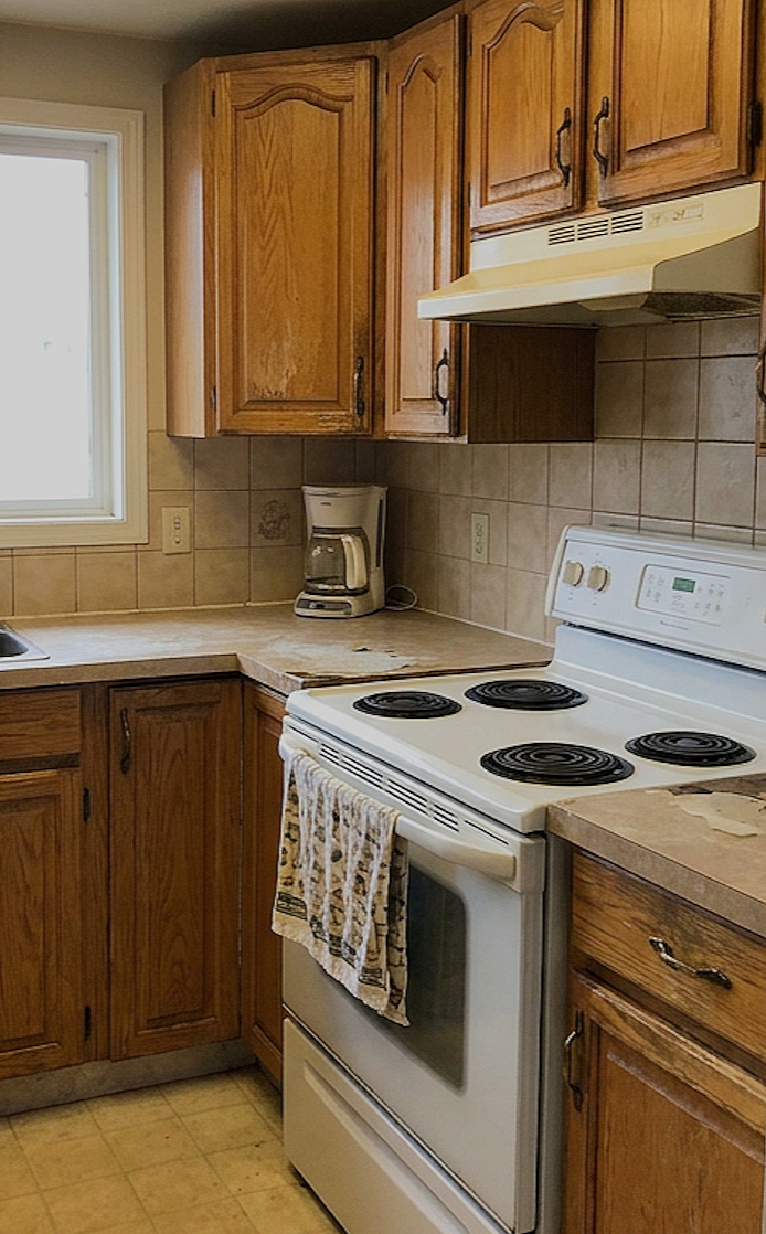 A kitchen corner with wooden cabinets, a window, a coffee maker, a stove with coil burners, and a towel hanging on the oven handle.
