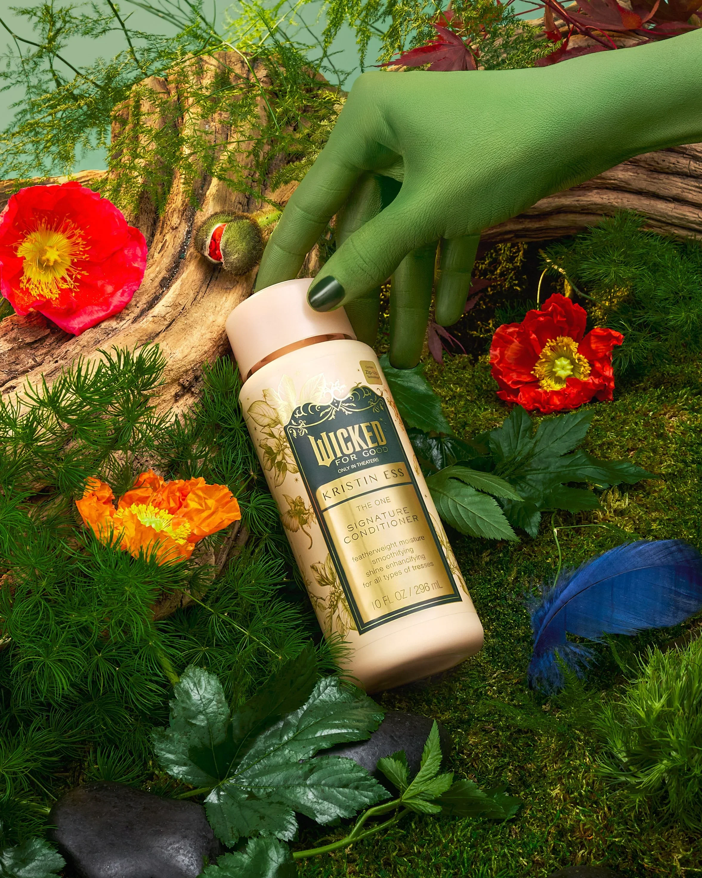 A plant-based scene featuring a large green hand with painted nails holding a bottle of Kristin Ess Lucky for Good conditioner amidst lush green plants, red and orange flowers, moss, rocks, and wood logs.