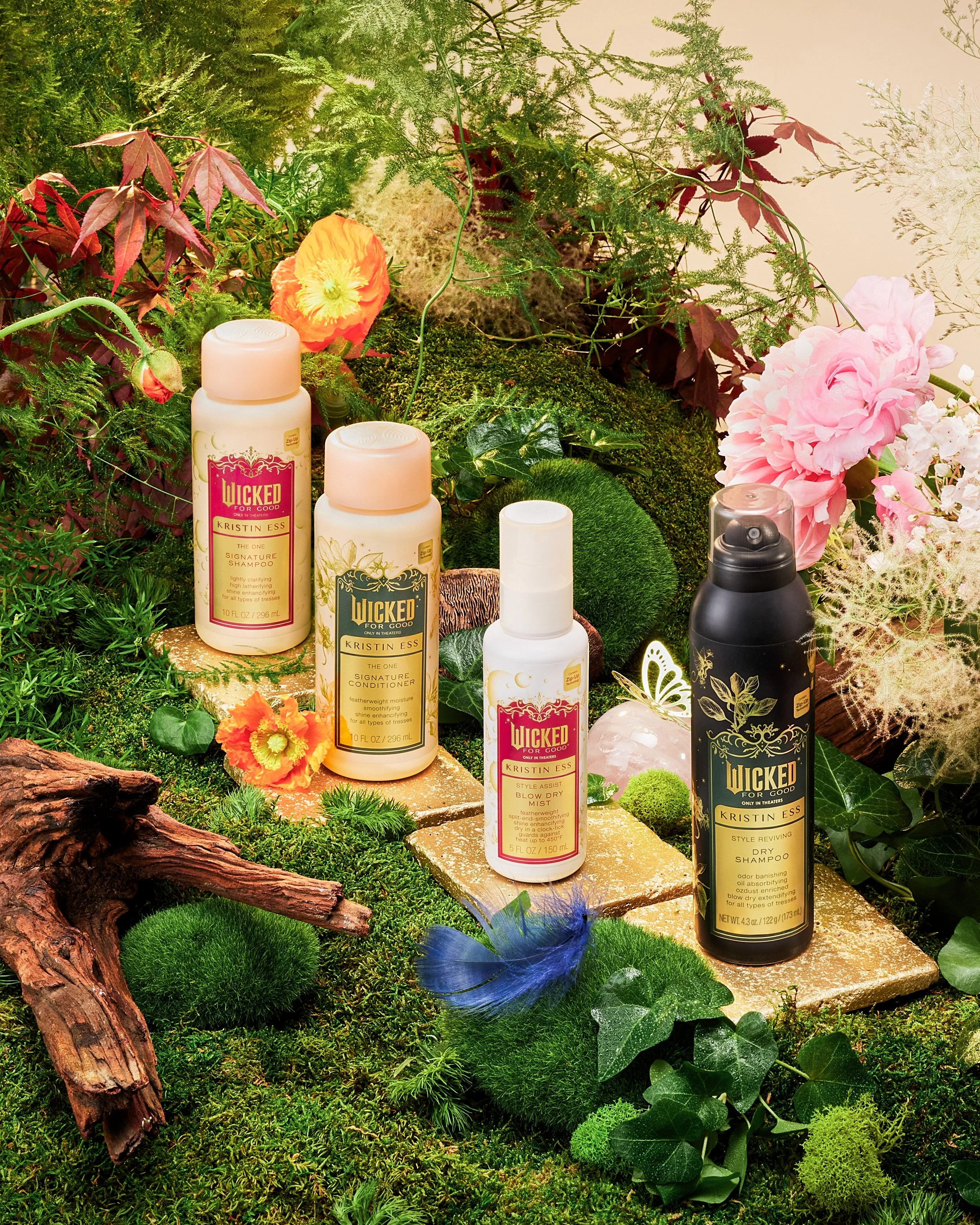A display of hair care products surrounded by lush green plants, moss, and flowers, with a small piece of wood and decorative elements.
