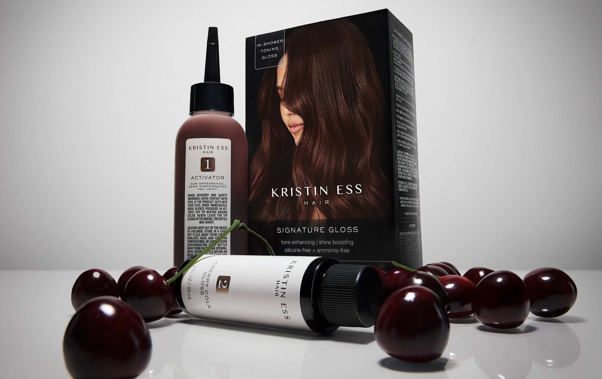 Hair care products packaging with a model's face on the box and two bottles, surrounded by cherries, on a white background.