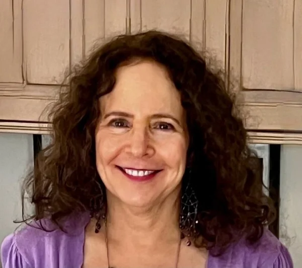 Smiling woman with curly brown hair wearing a purple top and dangling earrings
